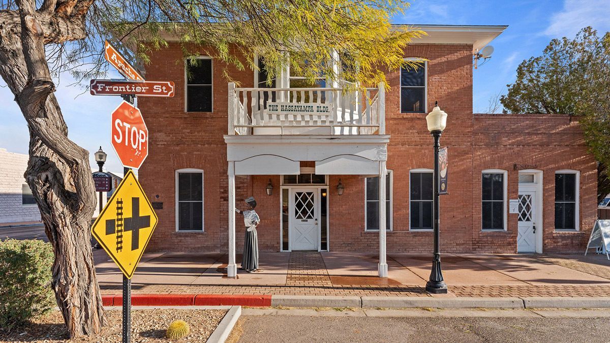 Brick building with white balcony, stop sign, and crossroad warning sign on a sunny street.