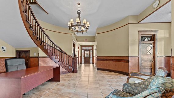 A spacious foyer with a curved staircase, a reception desk, patterned furniture, and a central chandelier.