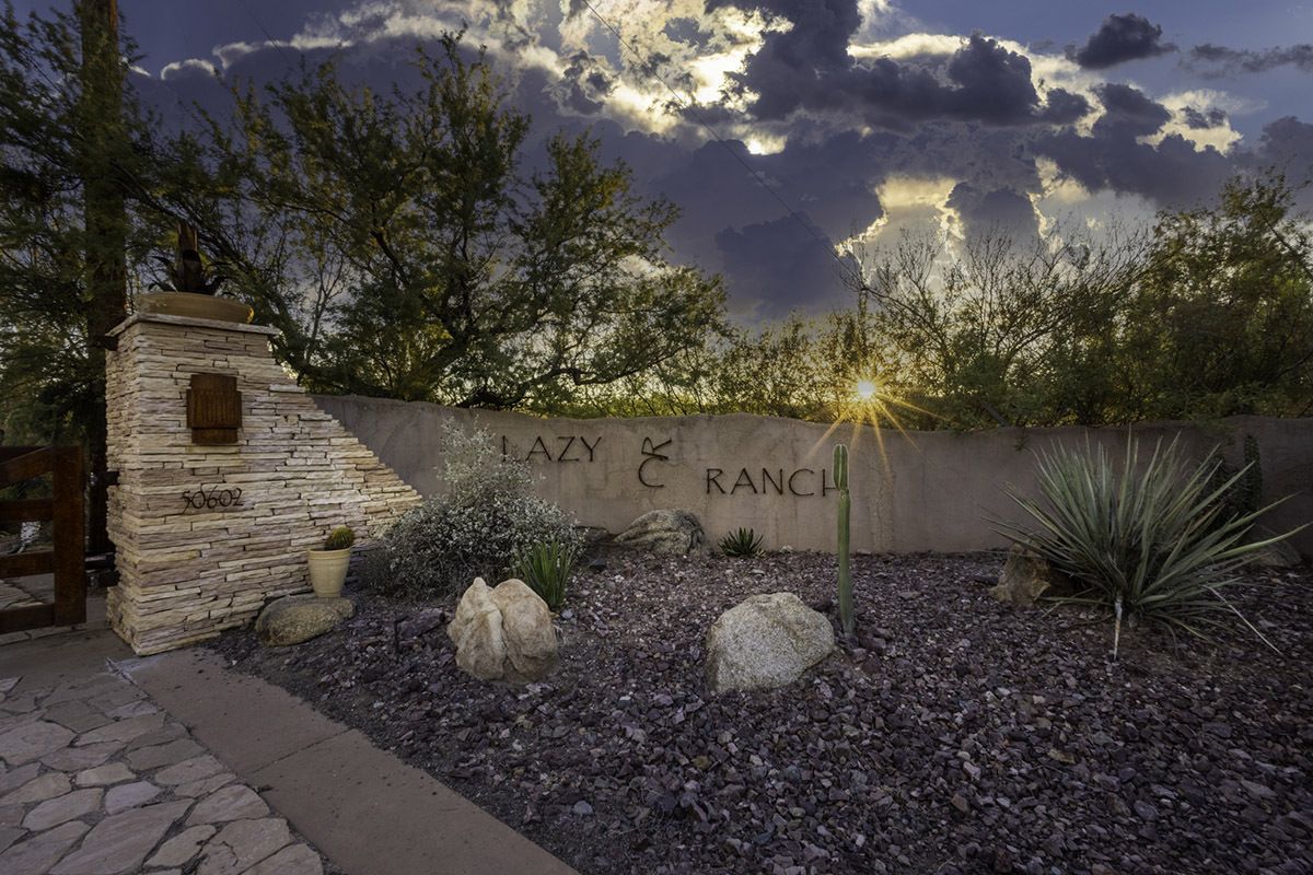 Stone entrance to "Lazy 8 Ranch" with desert plants and cloudy sky.