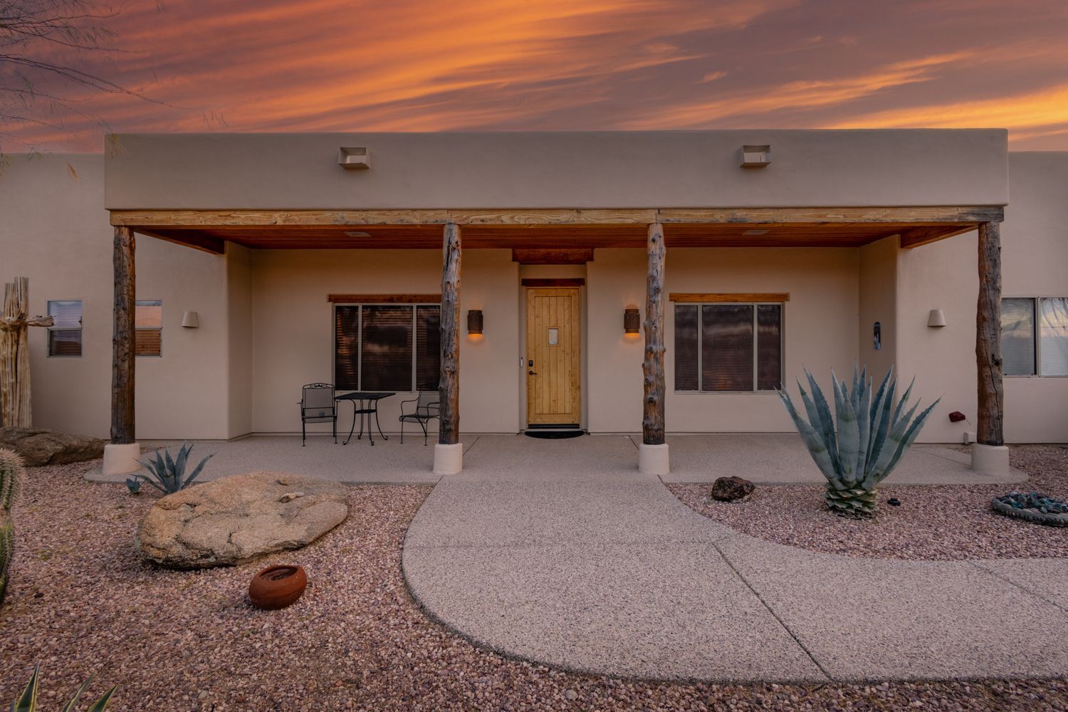 Desert home exterior with covered porch, wooden posts, and sunset sky.