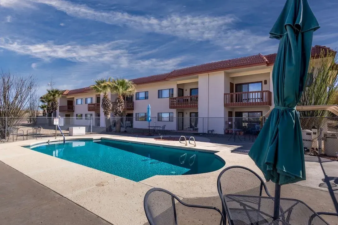 Spanish-style house with brick driveway, wooden beams, and palm trees against a blue sky.