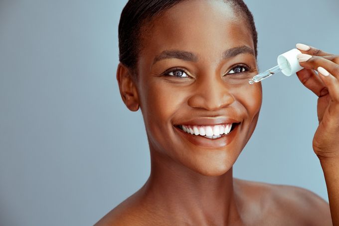 african american woman applying oil to cheek while smiling