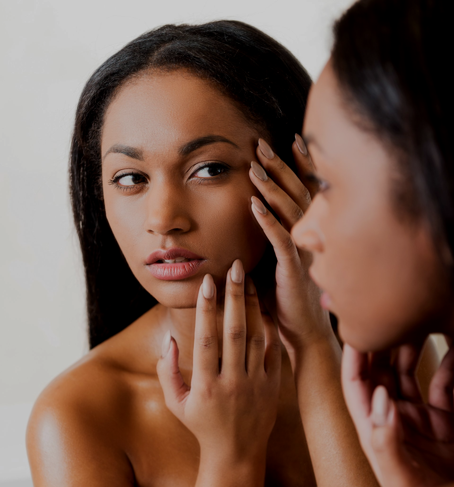 african american woman looking at acne on cheeks in mirror