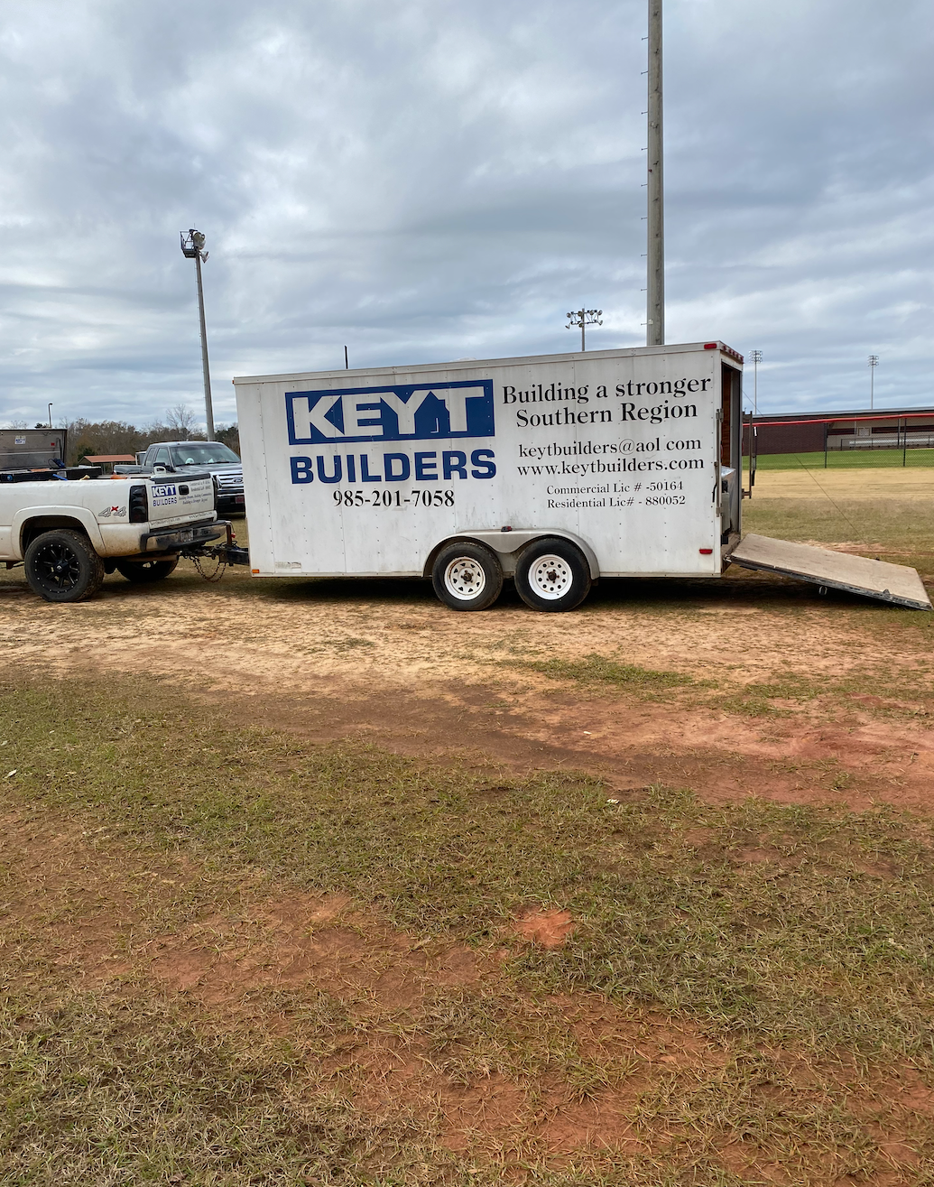 A keyt builders trailer is parked in a grassy field next to a truck.