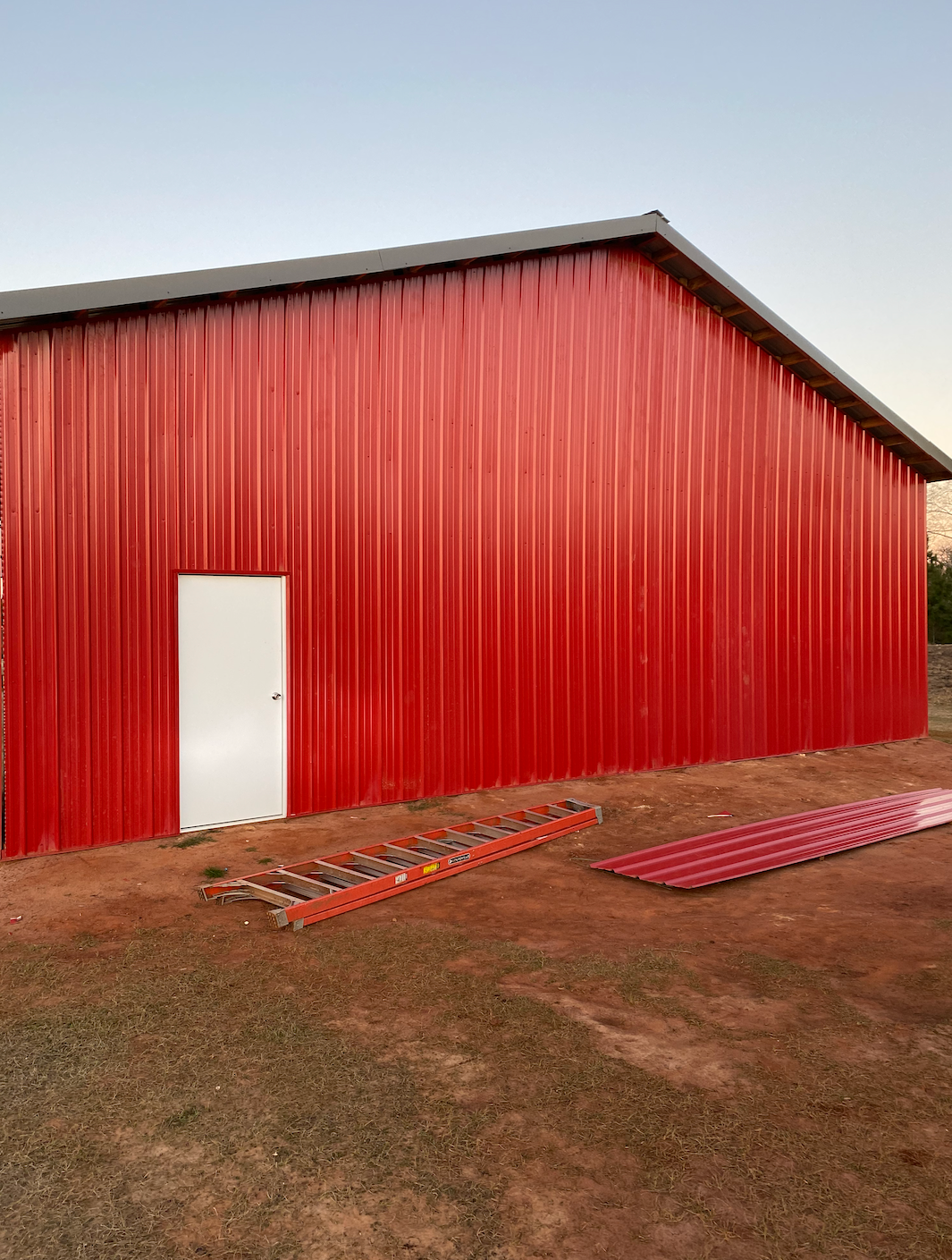 A large red barn with a white door and a ladder in front of it.