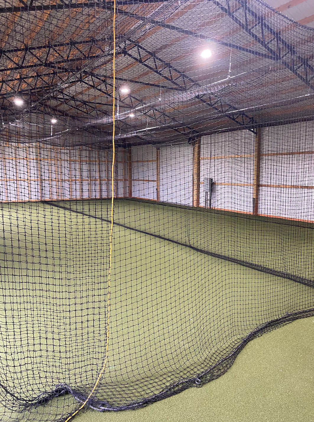 A large indoor baseball field with a net in the middle of it.