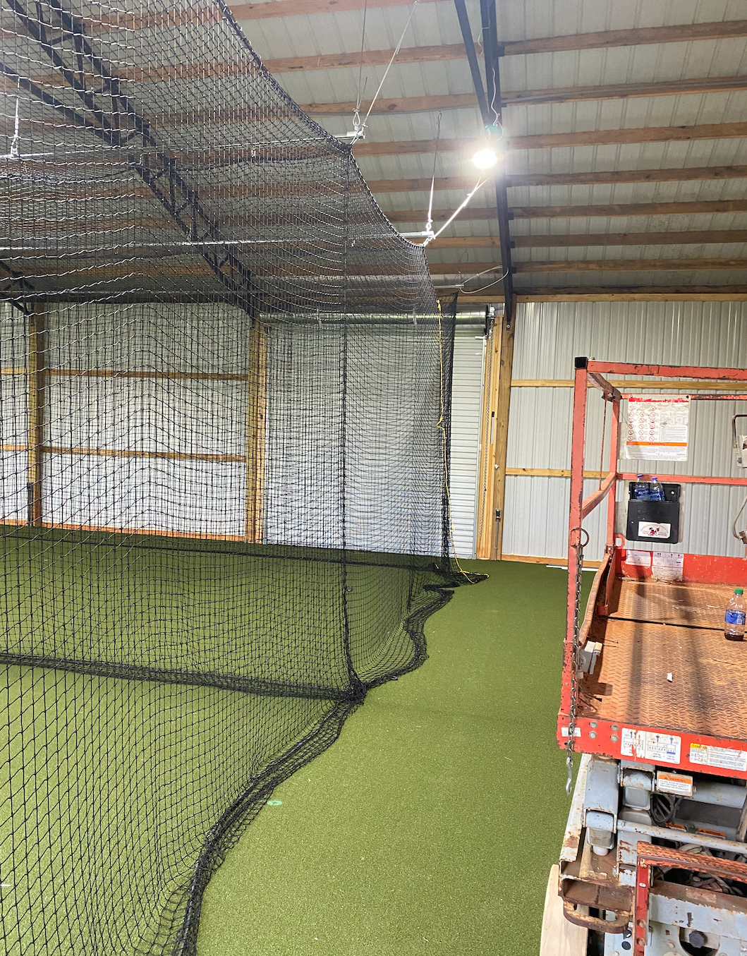 A ceiling fan is hanging from the ceiling of a baseball cage.