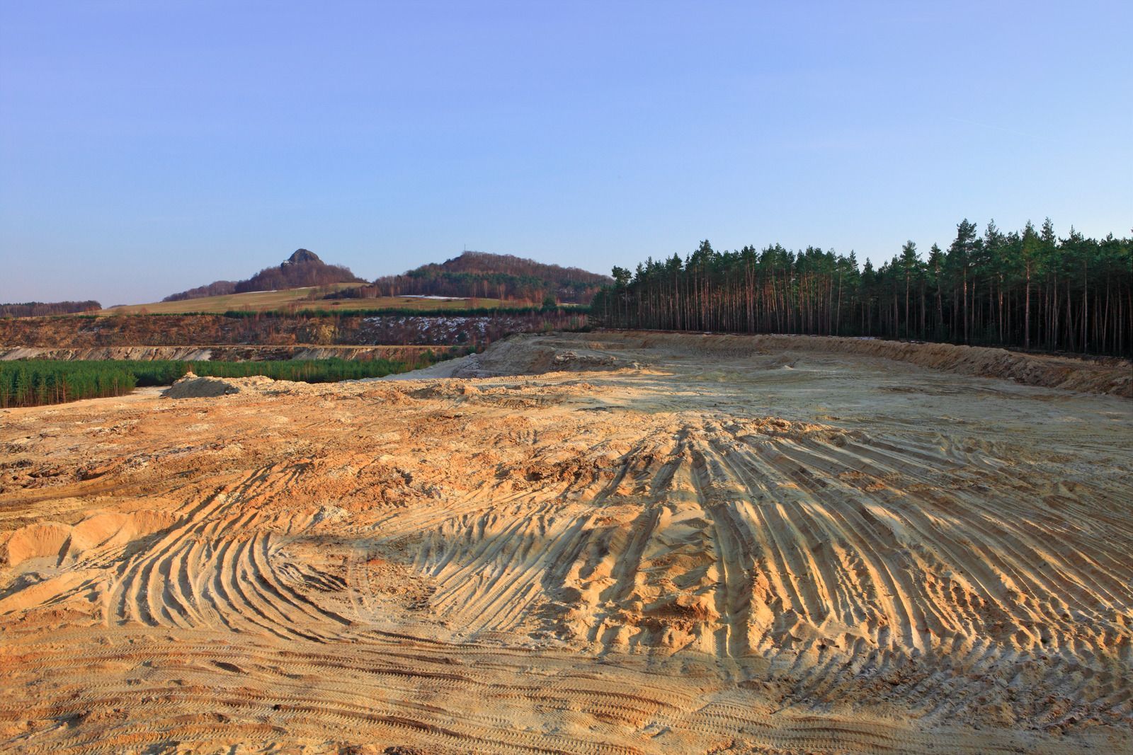 A dirt field with trees in the background and mountains in the background