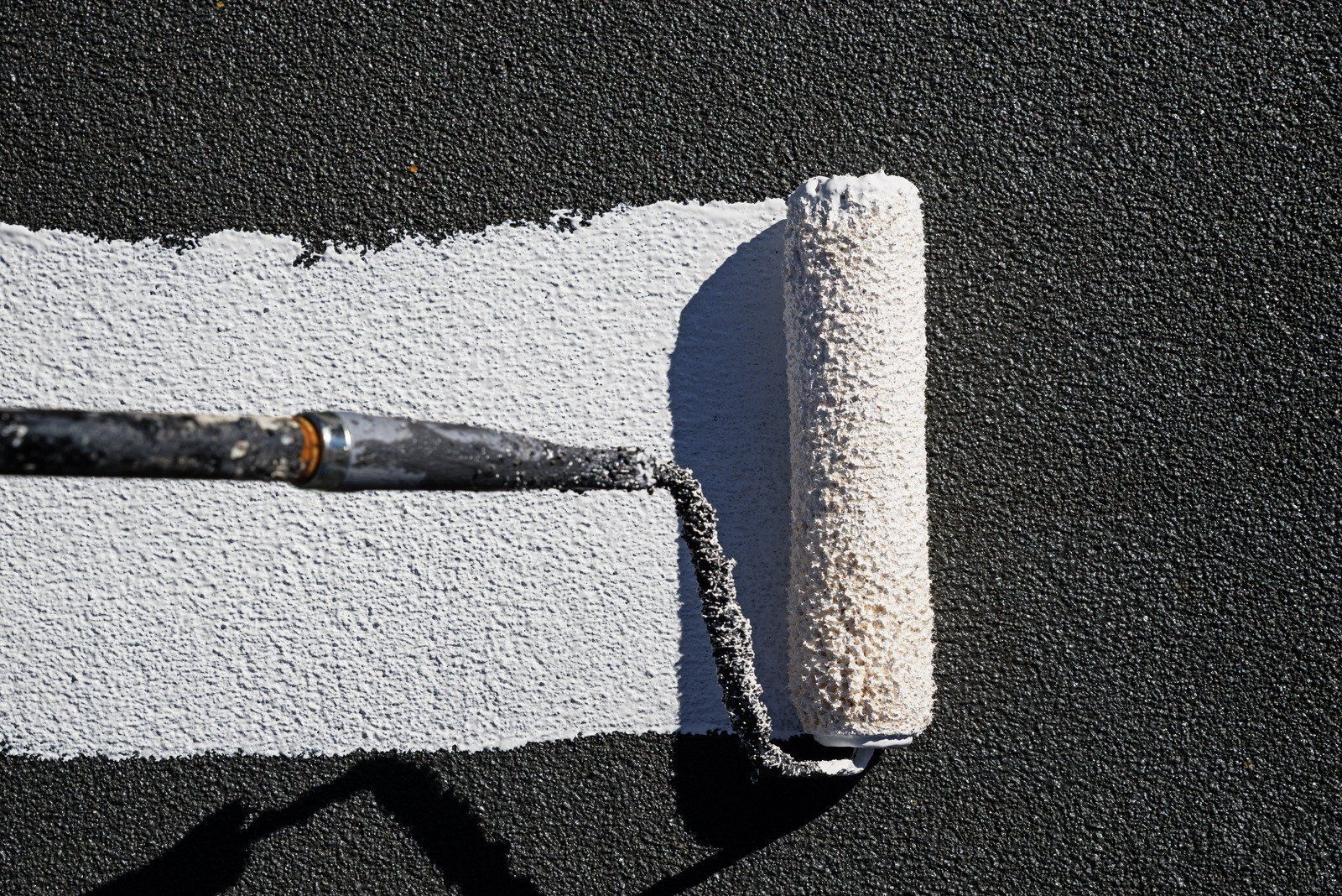 A paint roller is rolling white paint on a black surface.