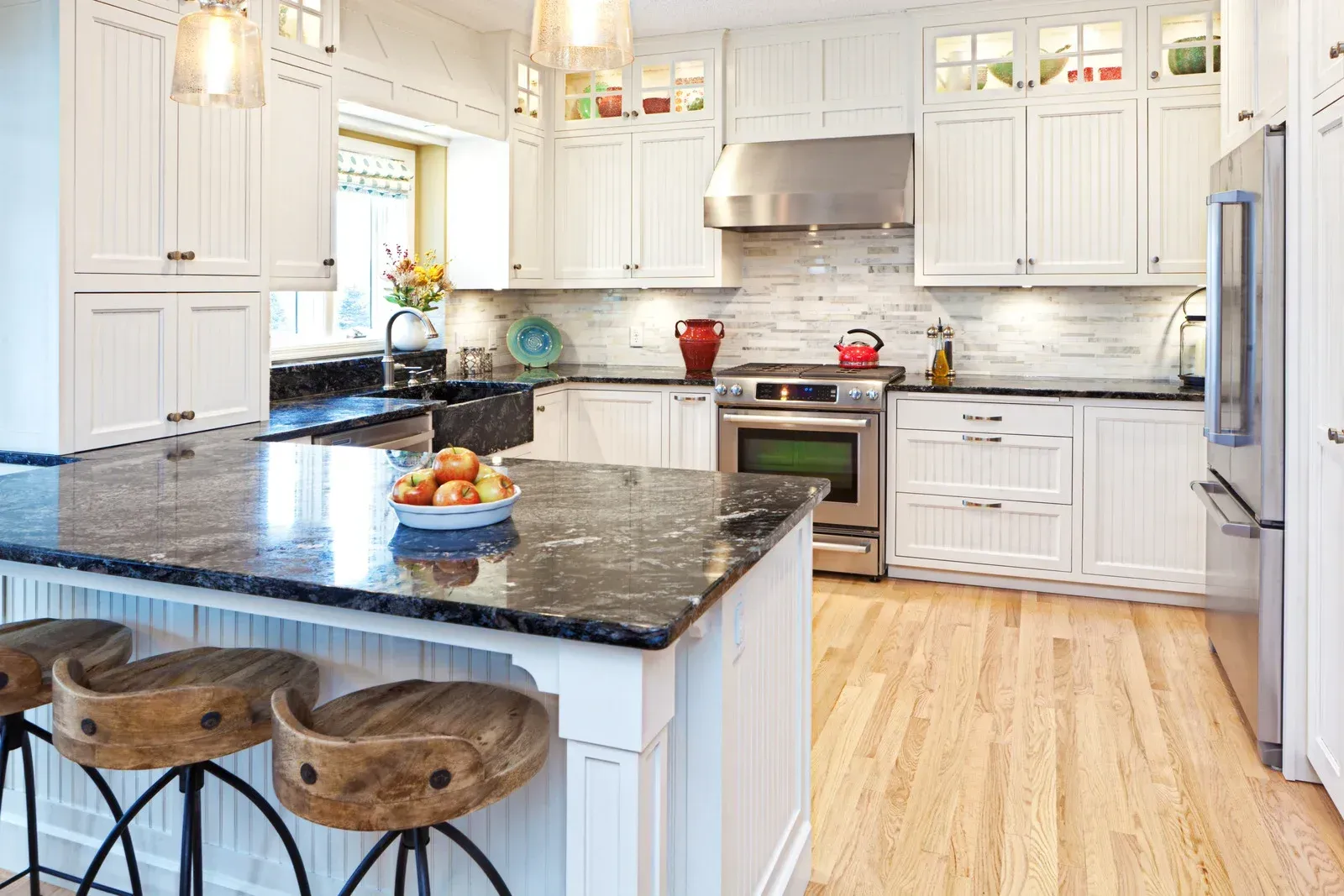 A kitchen with white cabinets , granite counter tops , stainless steel appliances and a large island.