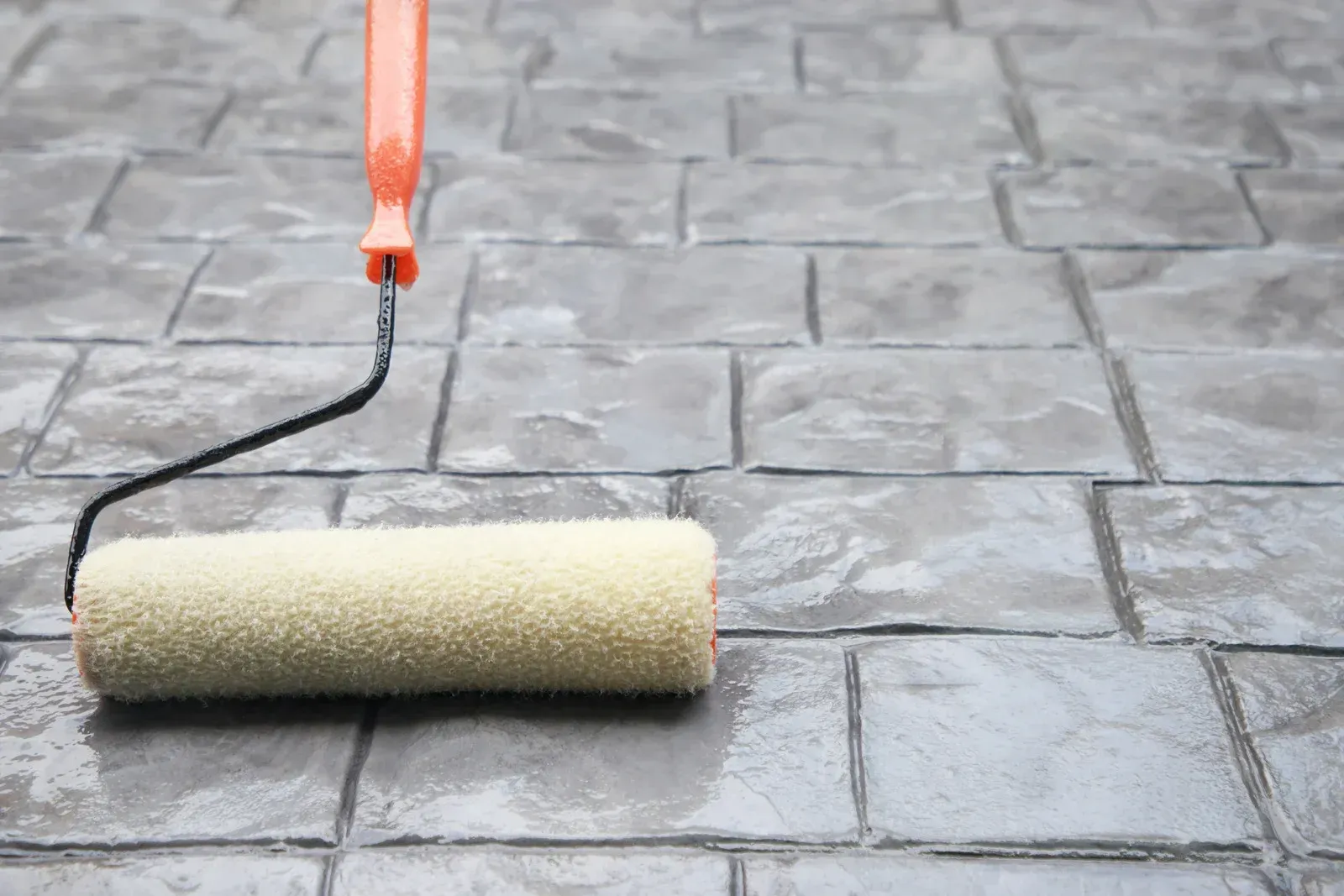A roller is being used to paint a brick floor.
