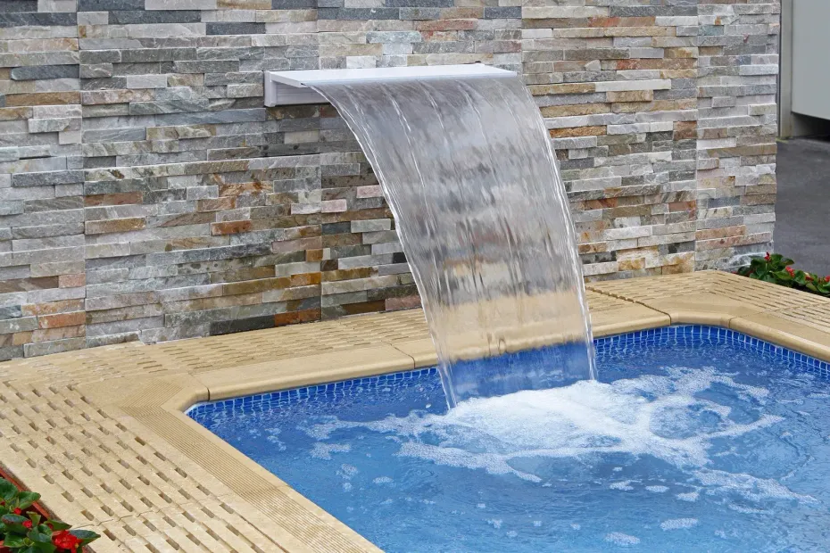 A waterfall is coming down the side of a swimming pool.