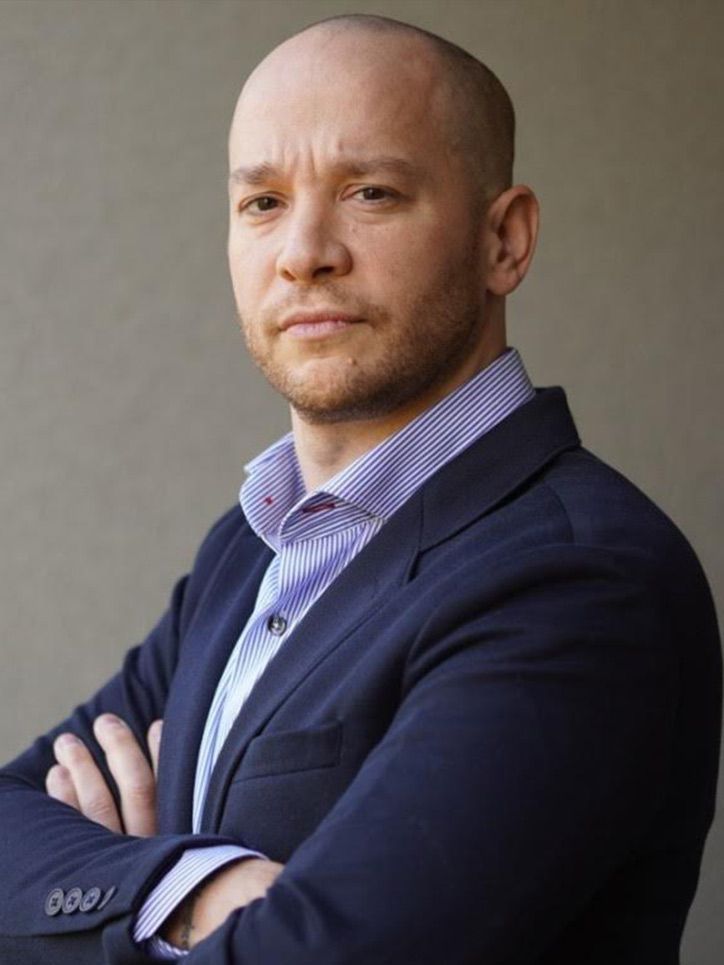 A bald man in a suit with his arms crossed