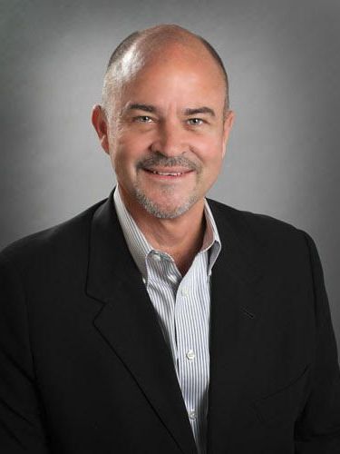 A man in a suit and striped shirt is smiling for the camera.