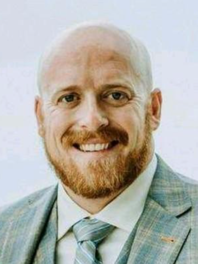 A bald man with a beard is wearing a suit and tie and smiling.
