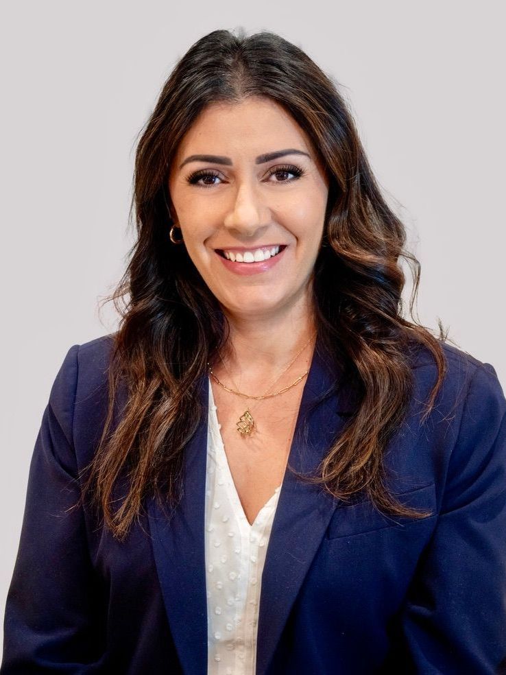 A woman wearing a pearl necklace and a black jacket is smiling for the camera.