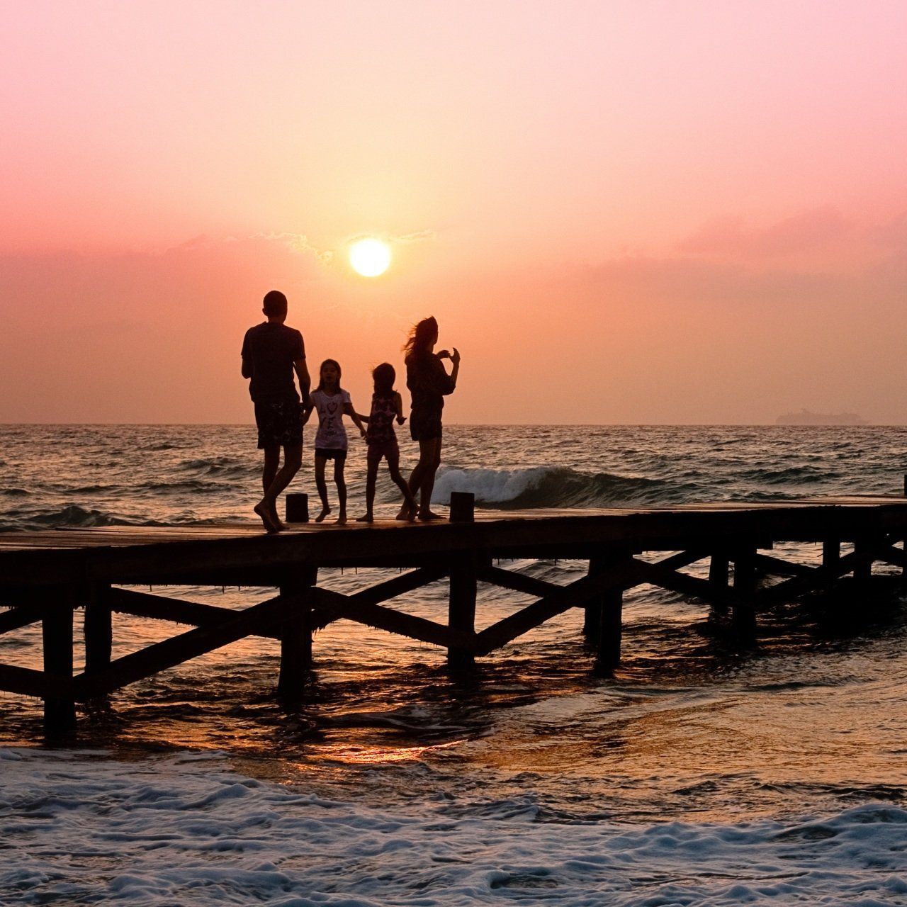 A family standing on a pier watching the sun set over the ocean