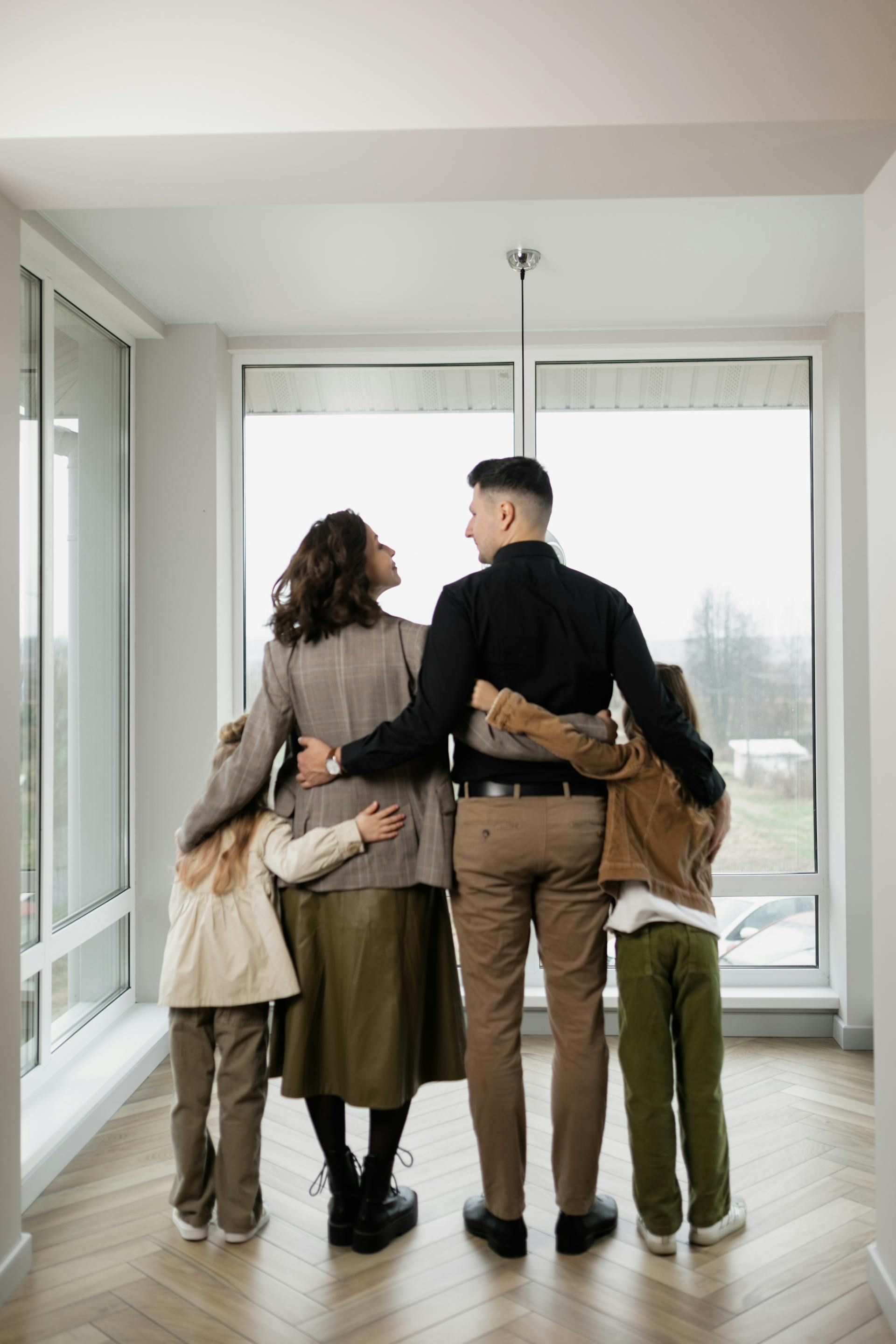 A family is standing in a room looking out a window.