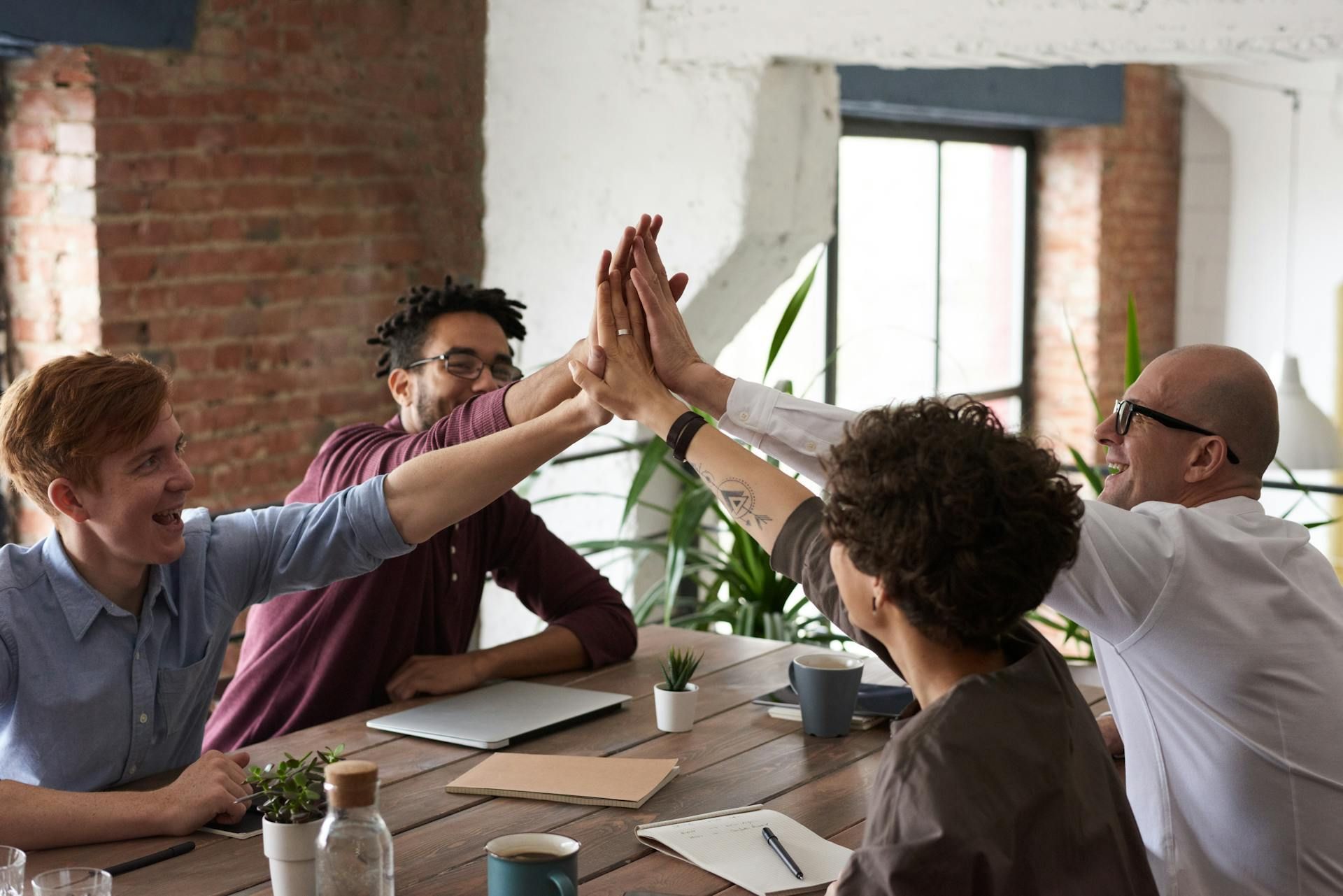 A group of people are giving each other a high five while sitting at a table.