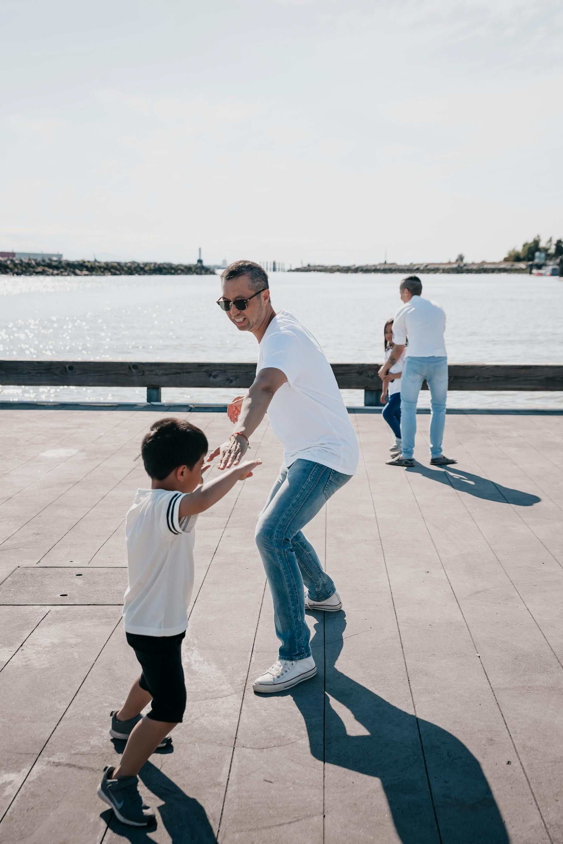 A man is holding a child 's hand while dancing on a pier.