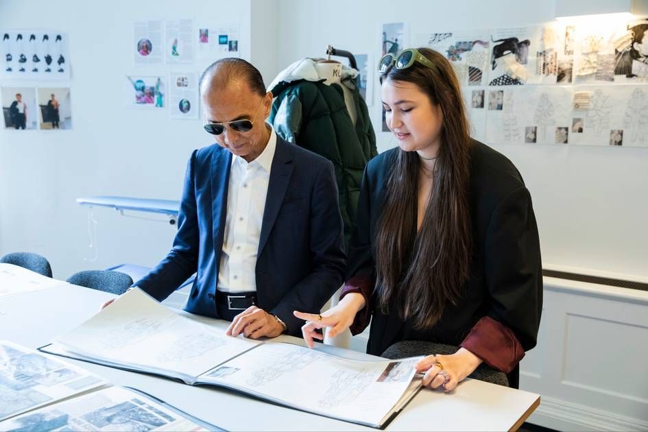 Man in suit seated, smiling in front of large window. Sunlight streams through the glass.
