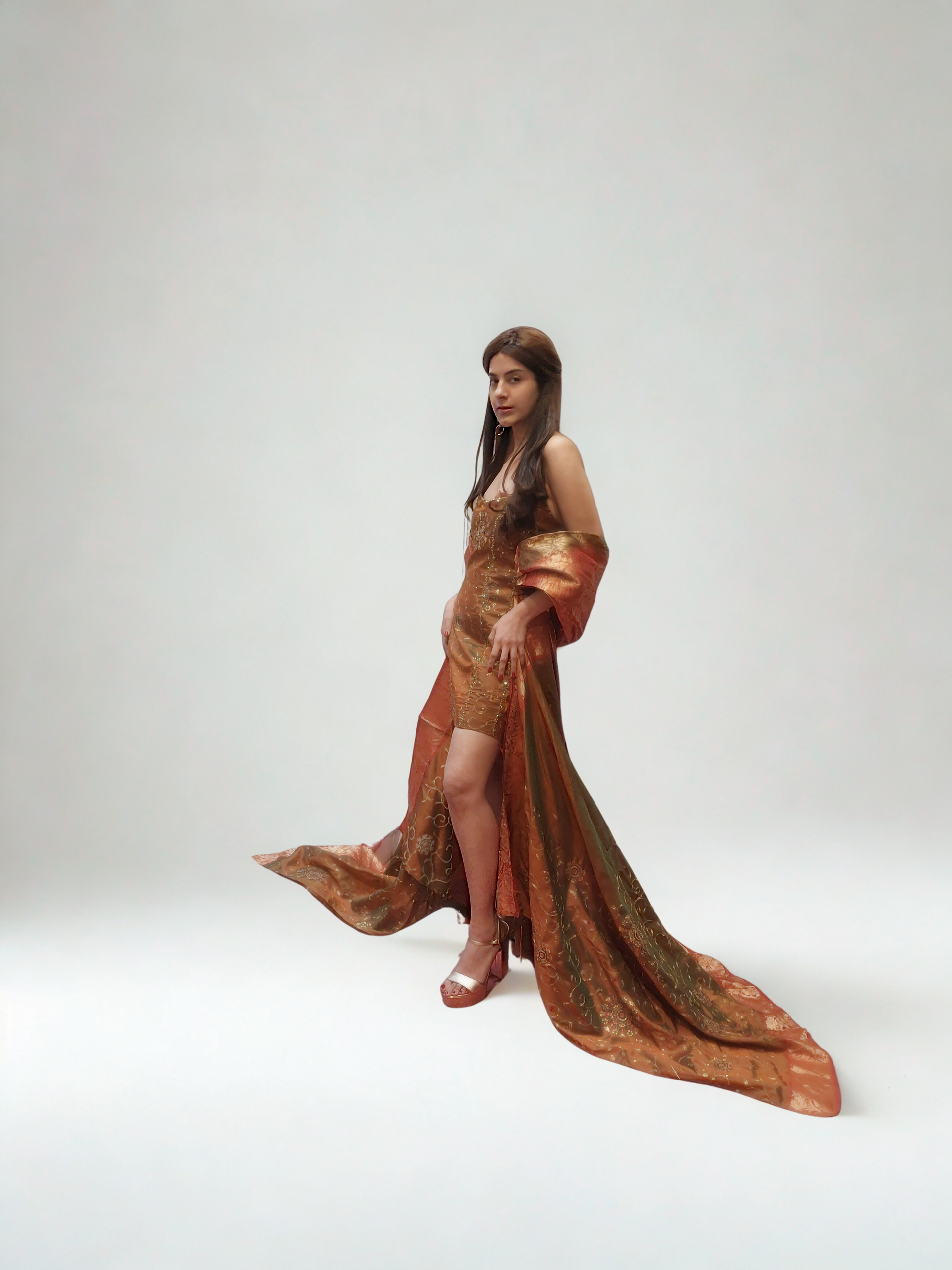 Woman in a flowing orange gown poses against a white backdrop.