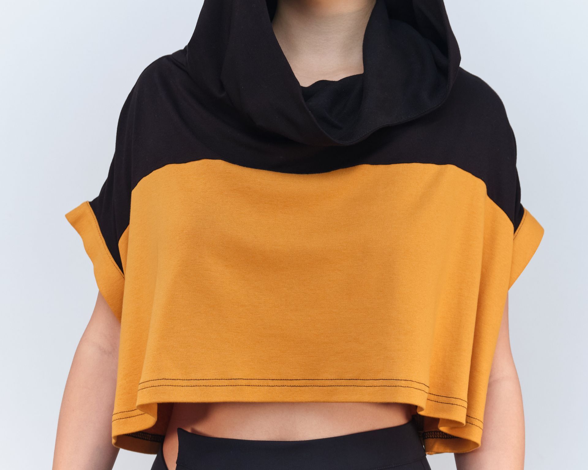 A woman wearing a black and yellow crop top with a hood
