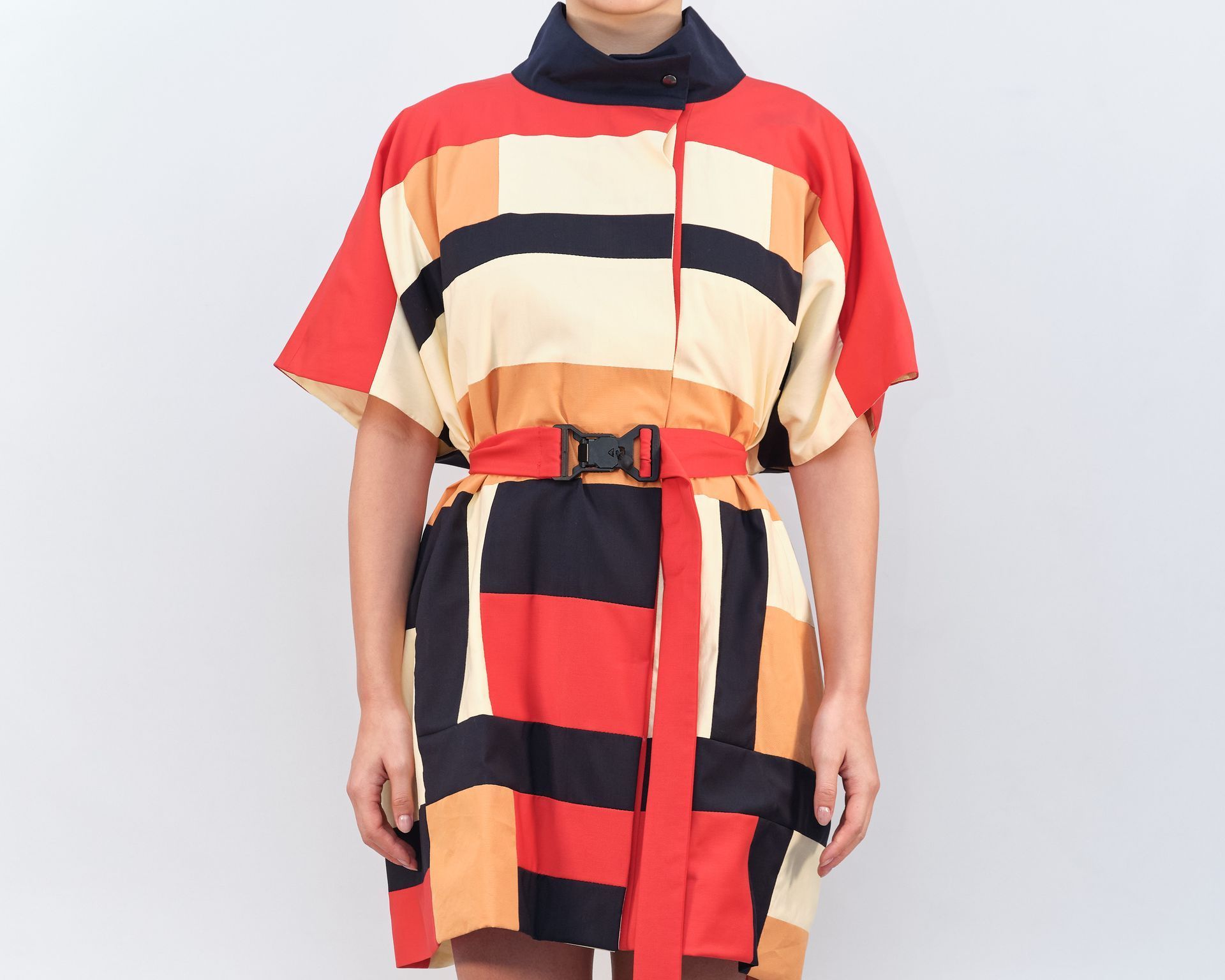 A woman in a colorful dress is standing in front of a white wall.