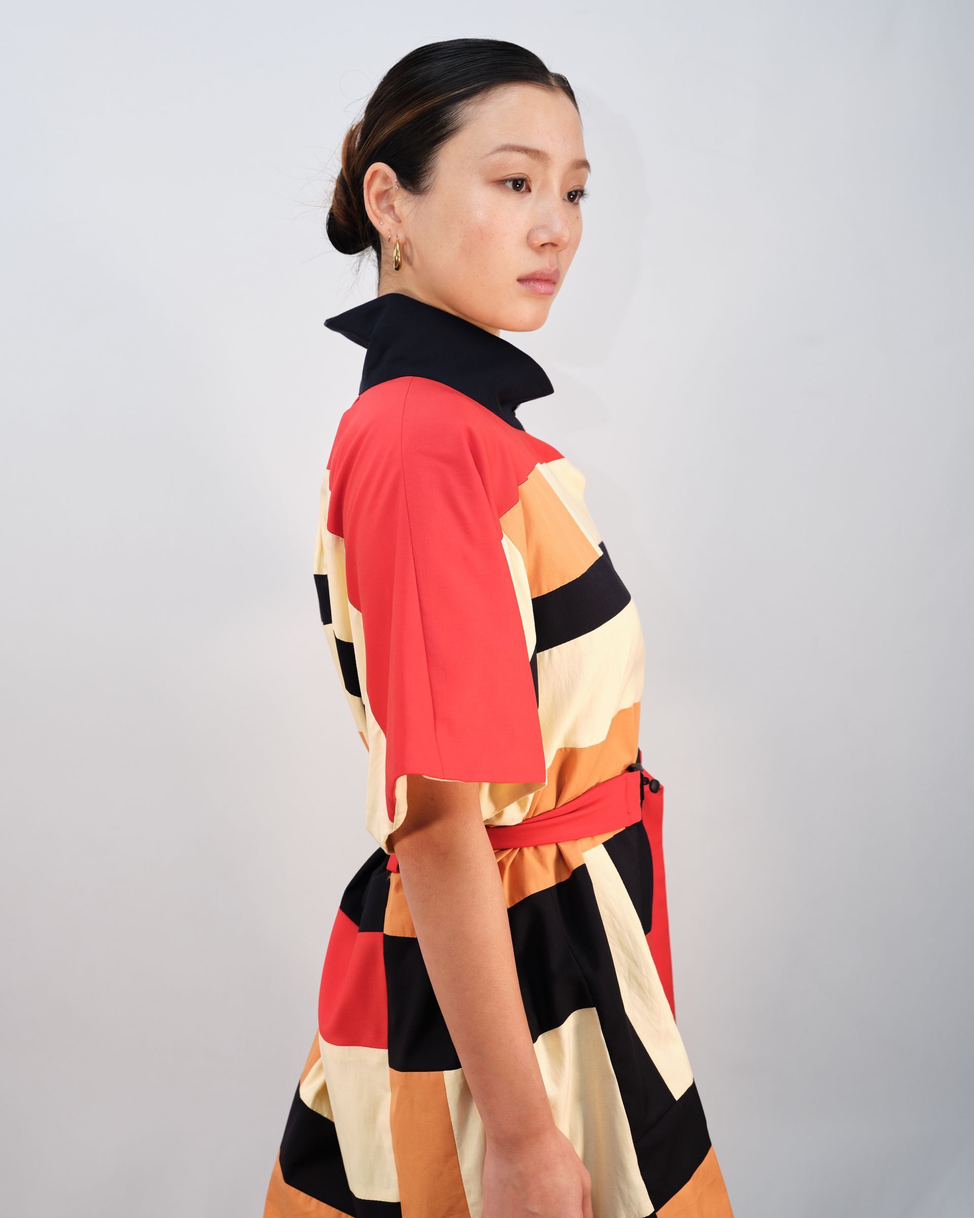 A woman in a colorful dress is standing in front of a white wall.