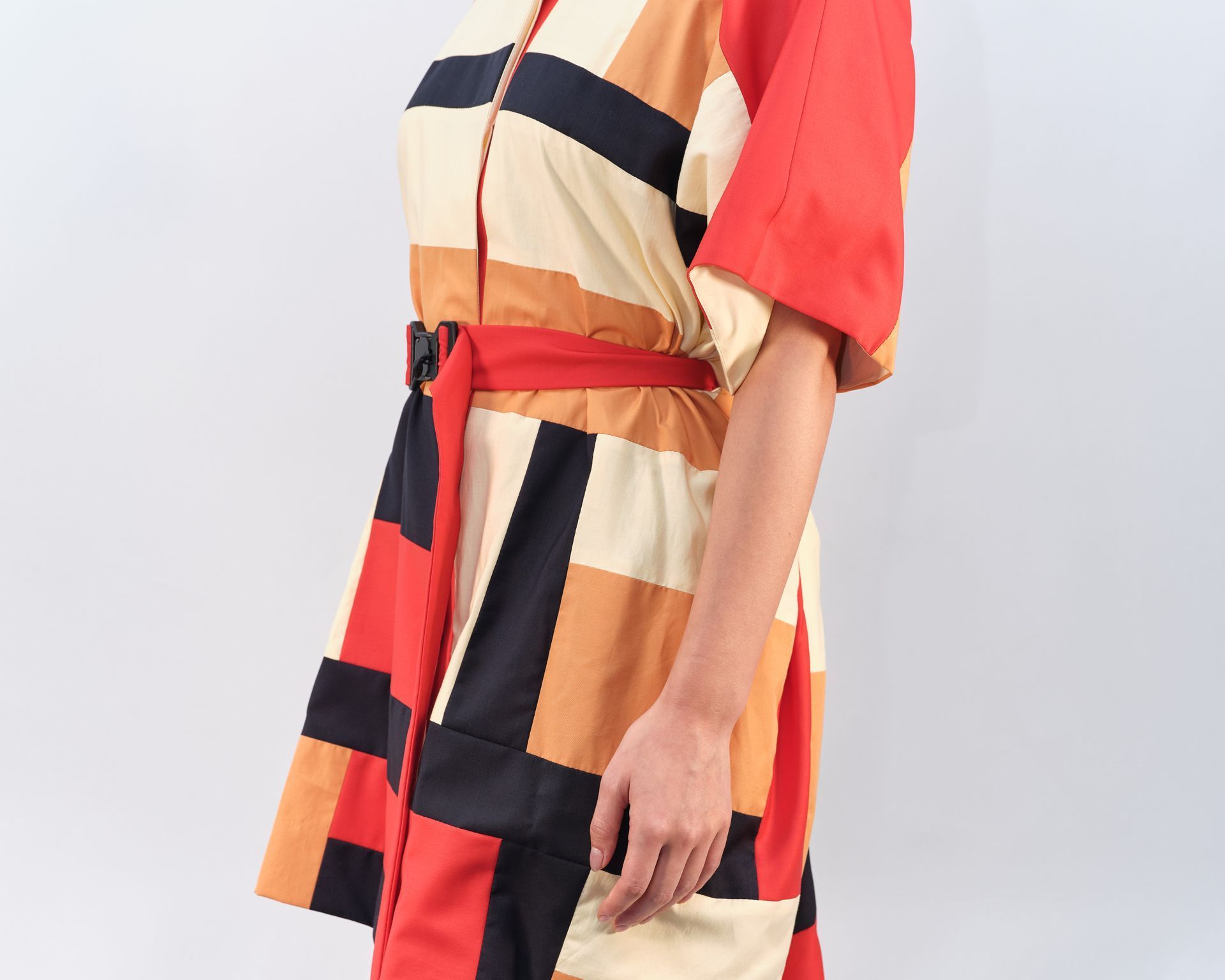 A woman is wearing a colorful dress with a red belt around her waist.