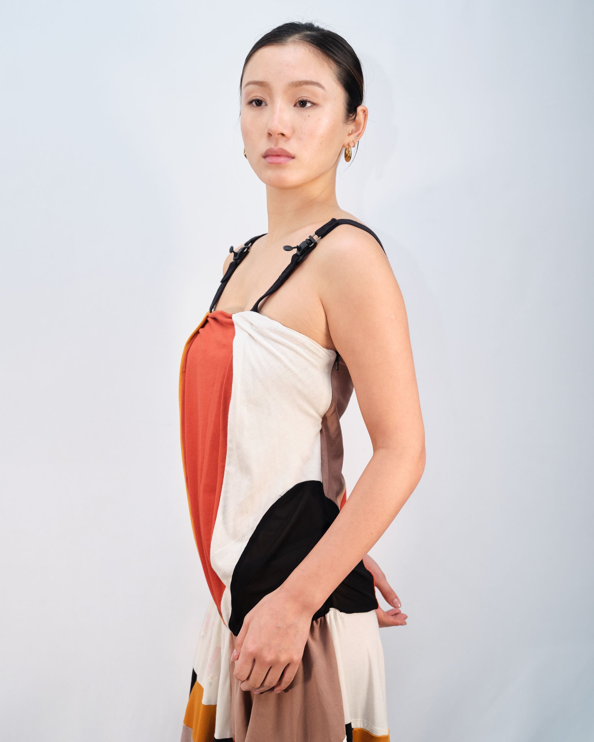 A woman in a colorful dress is standing in front of a white wall.