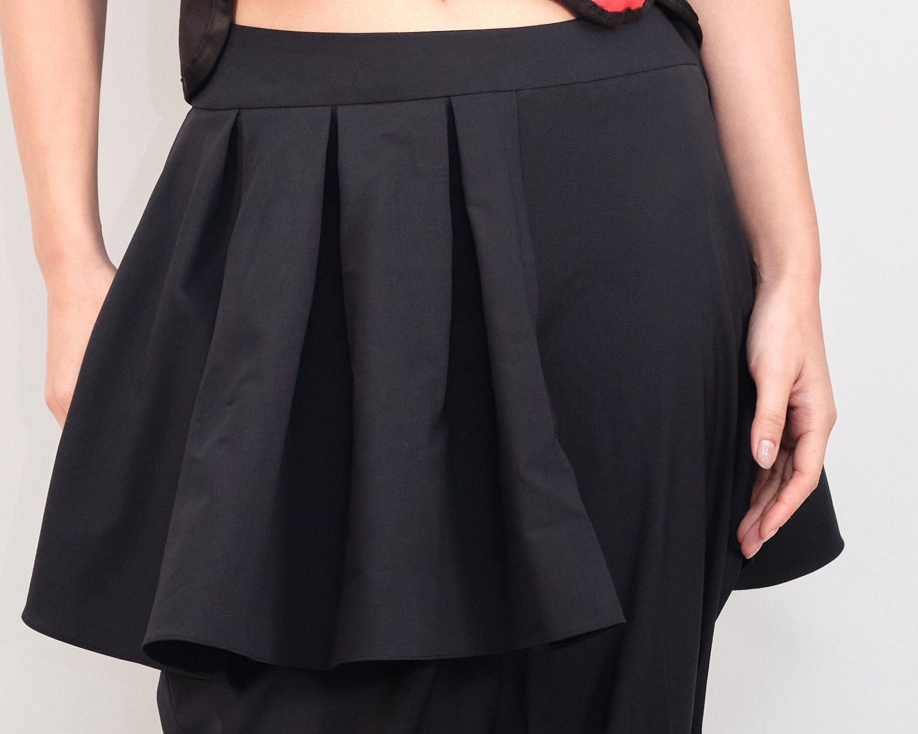 A woman wearing a black pleated skirt has her hands in her pockets