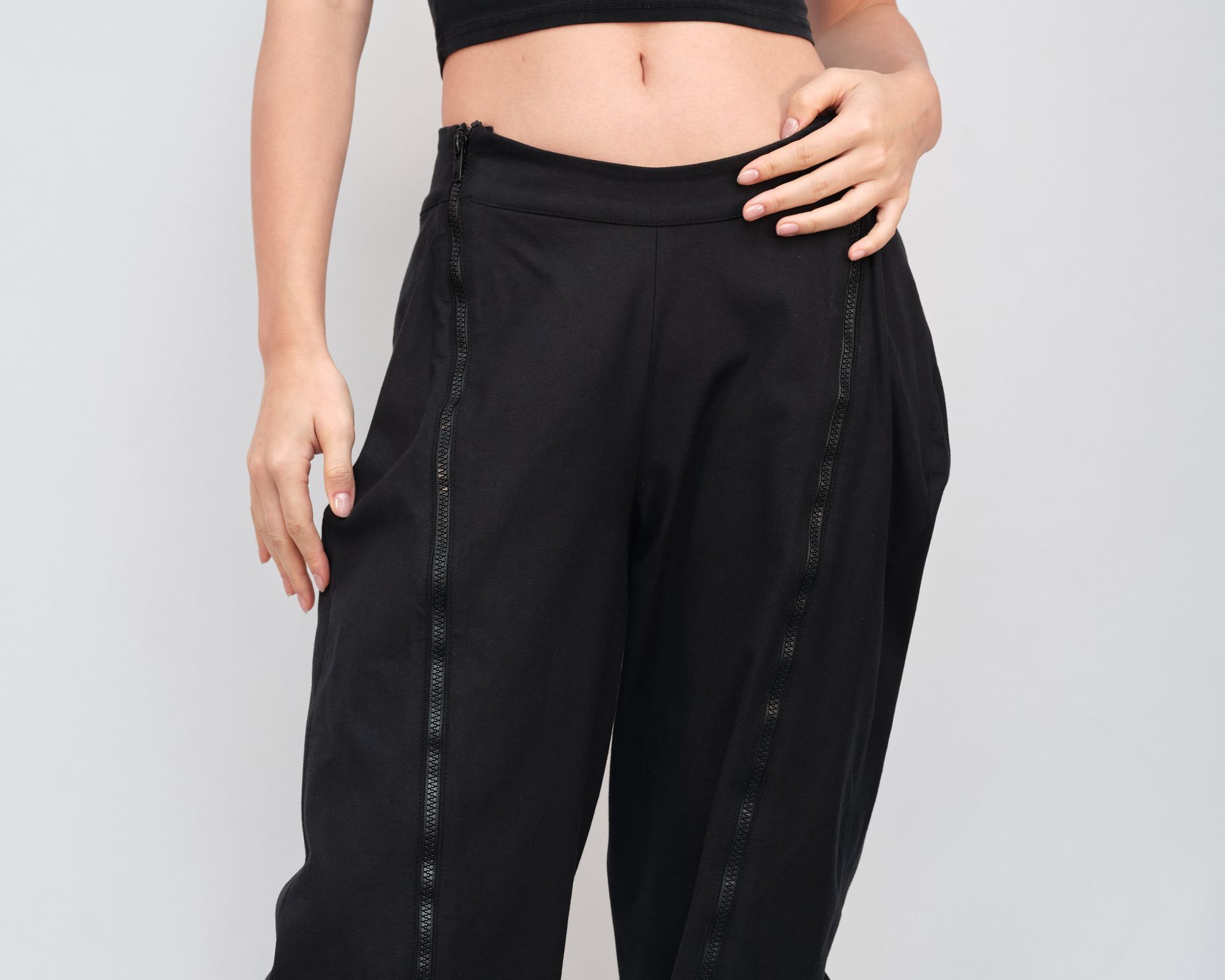 A woman in a crop top and black pants is standing with her hands on her hips.