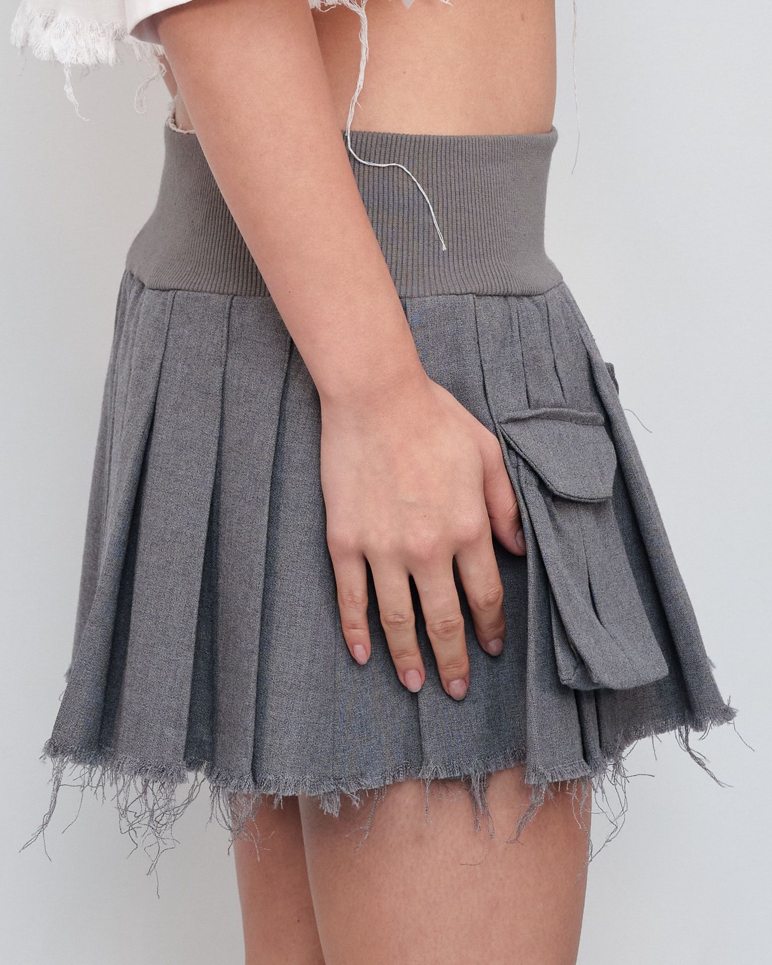 A woman is wearing a grey pleated skirt with pockets