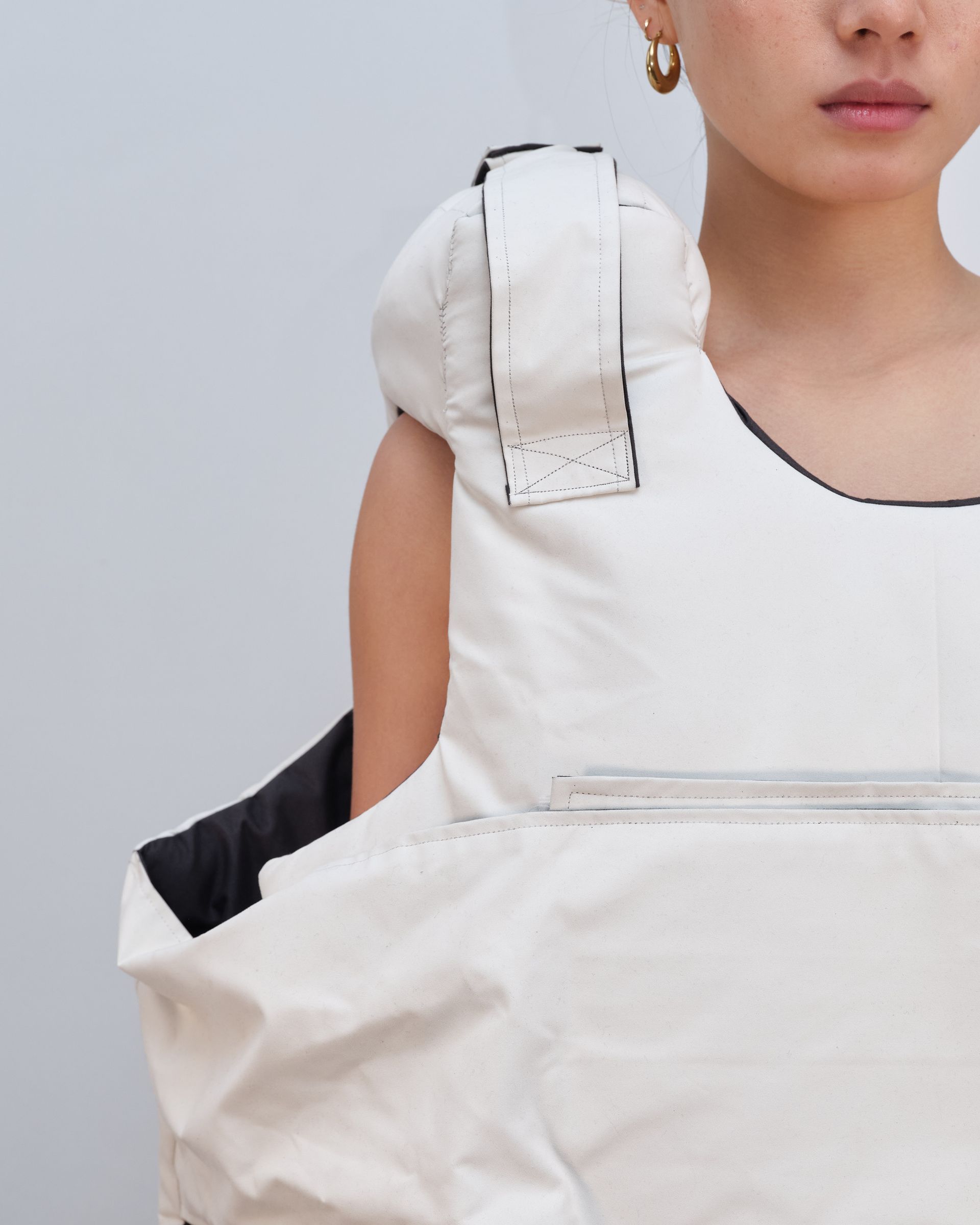 A woman is wearing a white vest and earrings