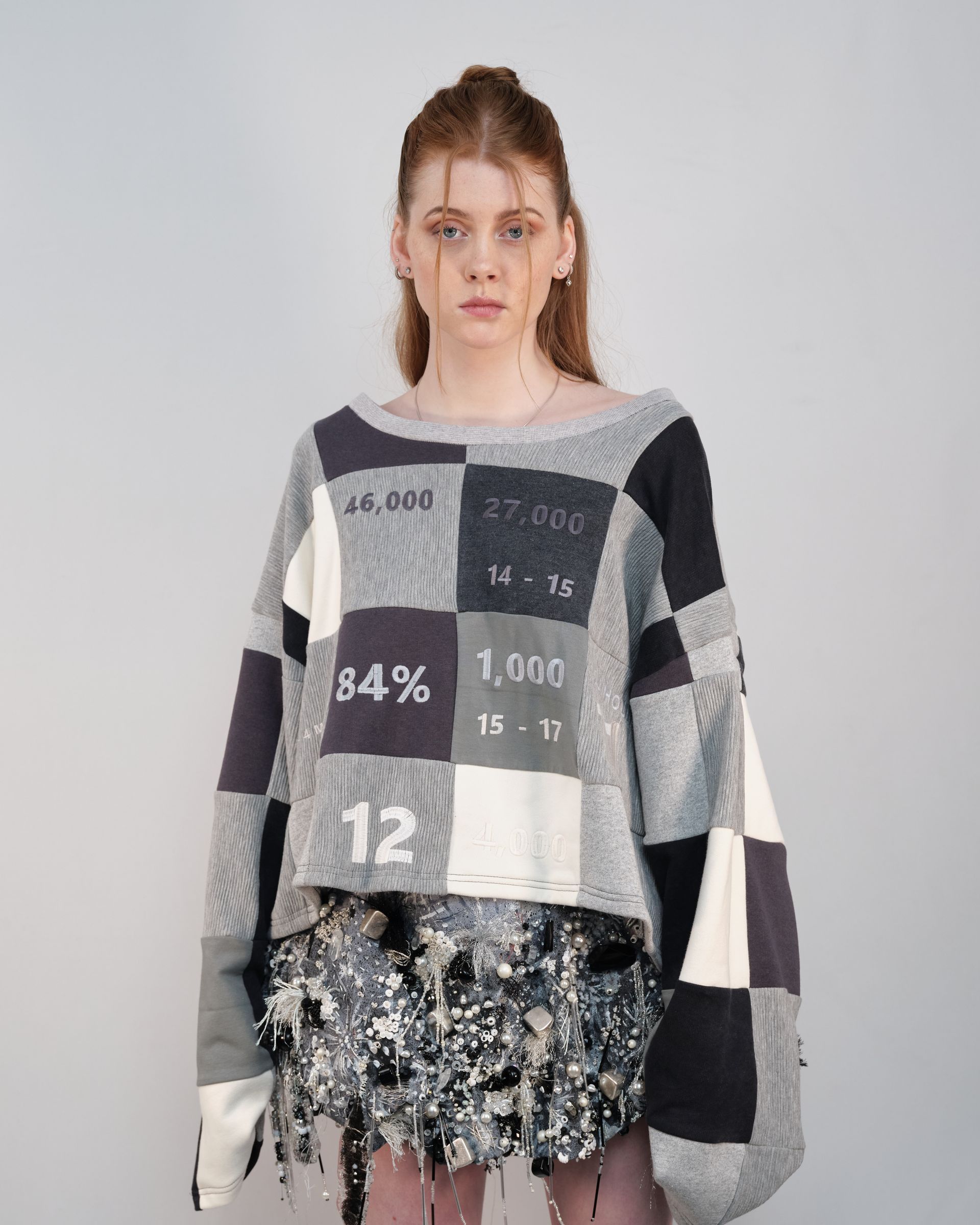 A woman is wearing a patchwork sweater and a checkered skirt.