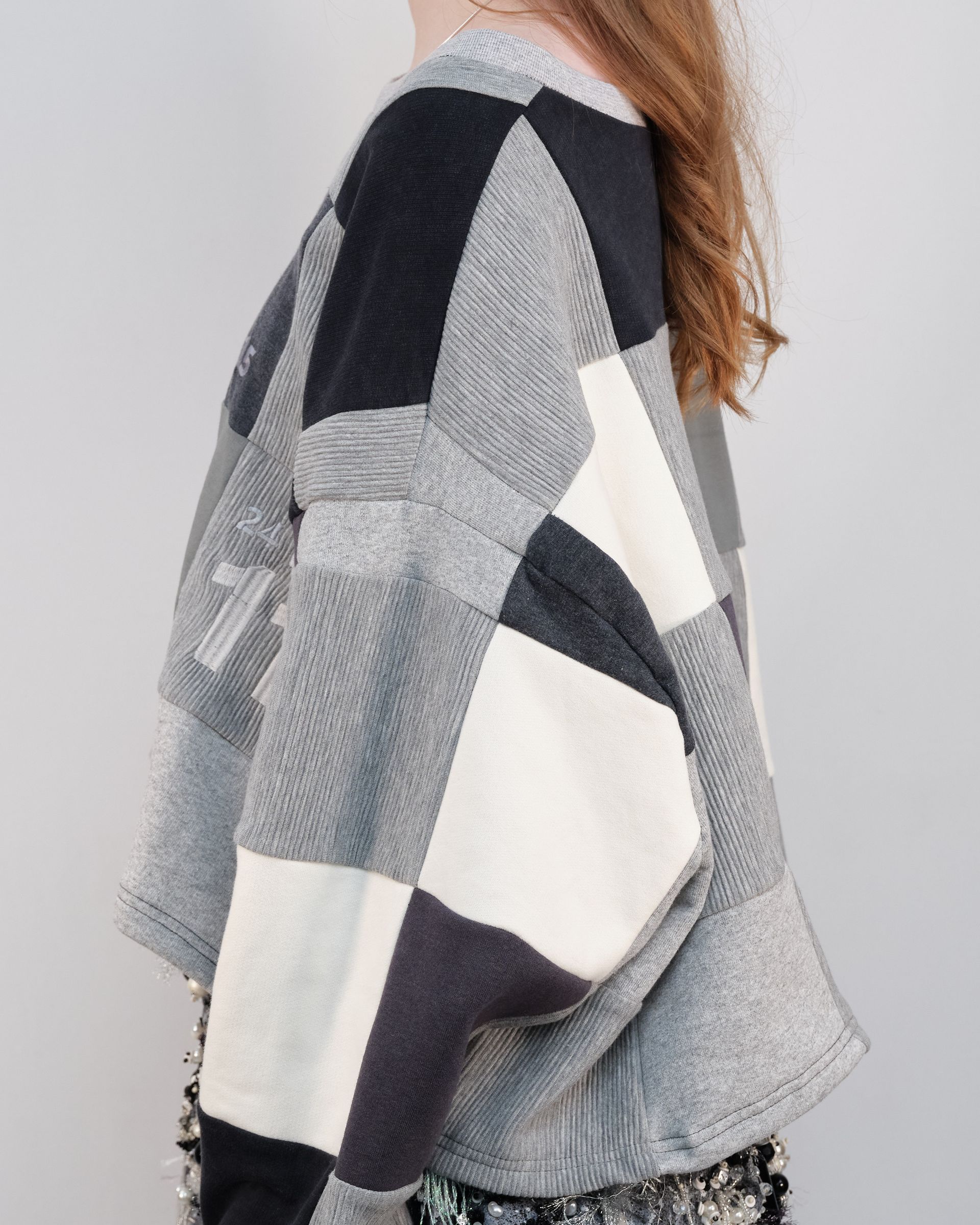 A woman is wearing a patchwork sweater and a checkered skirt.