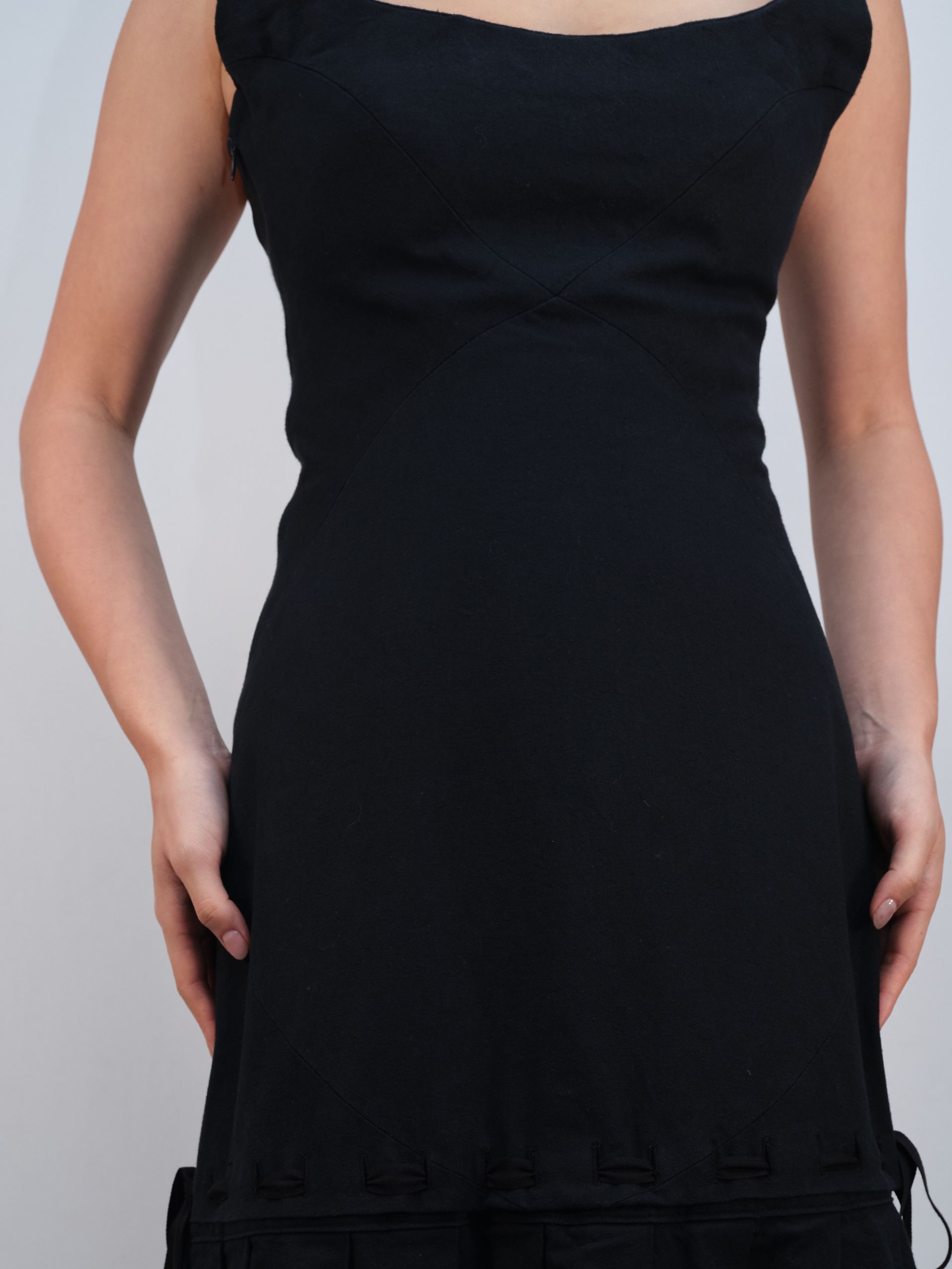 A woman in a black dress is standing with her hands in her pockets