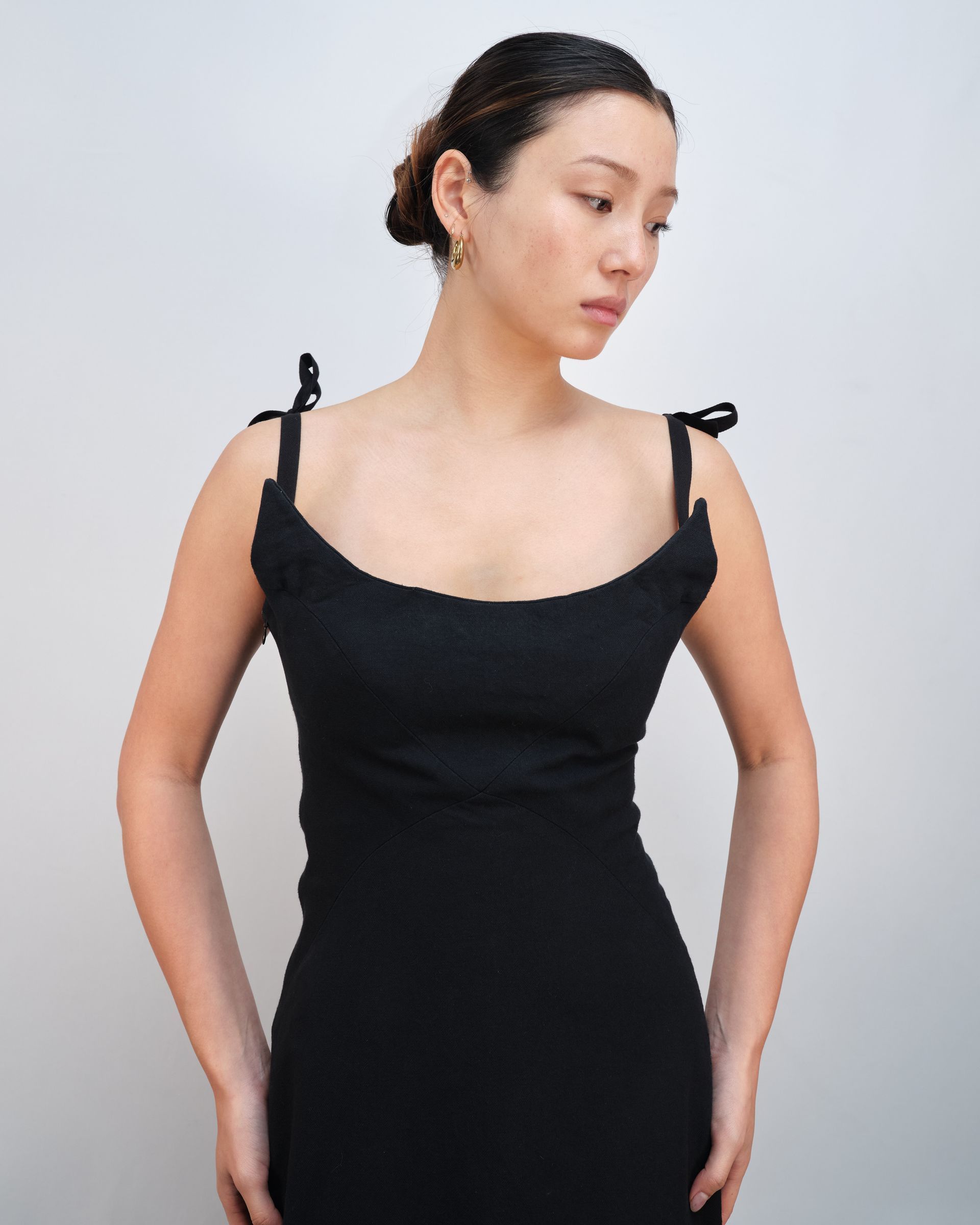 A woman in a black dress is standing in front of a white wall