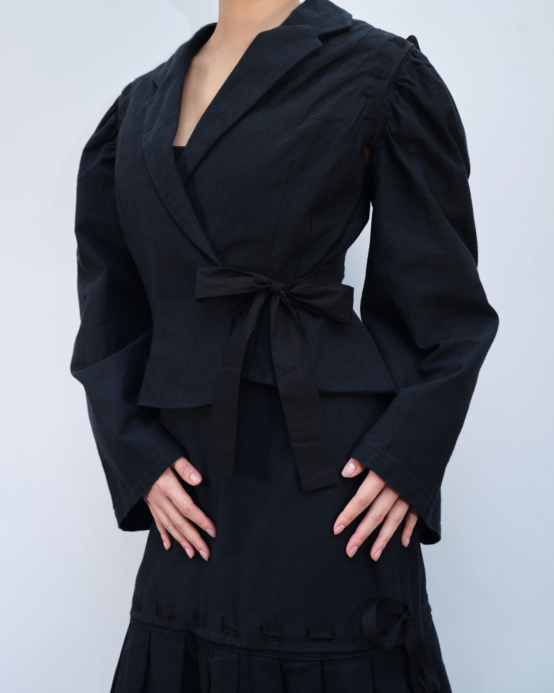 A woman is wearing a black jacket and skirt