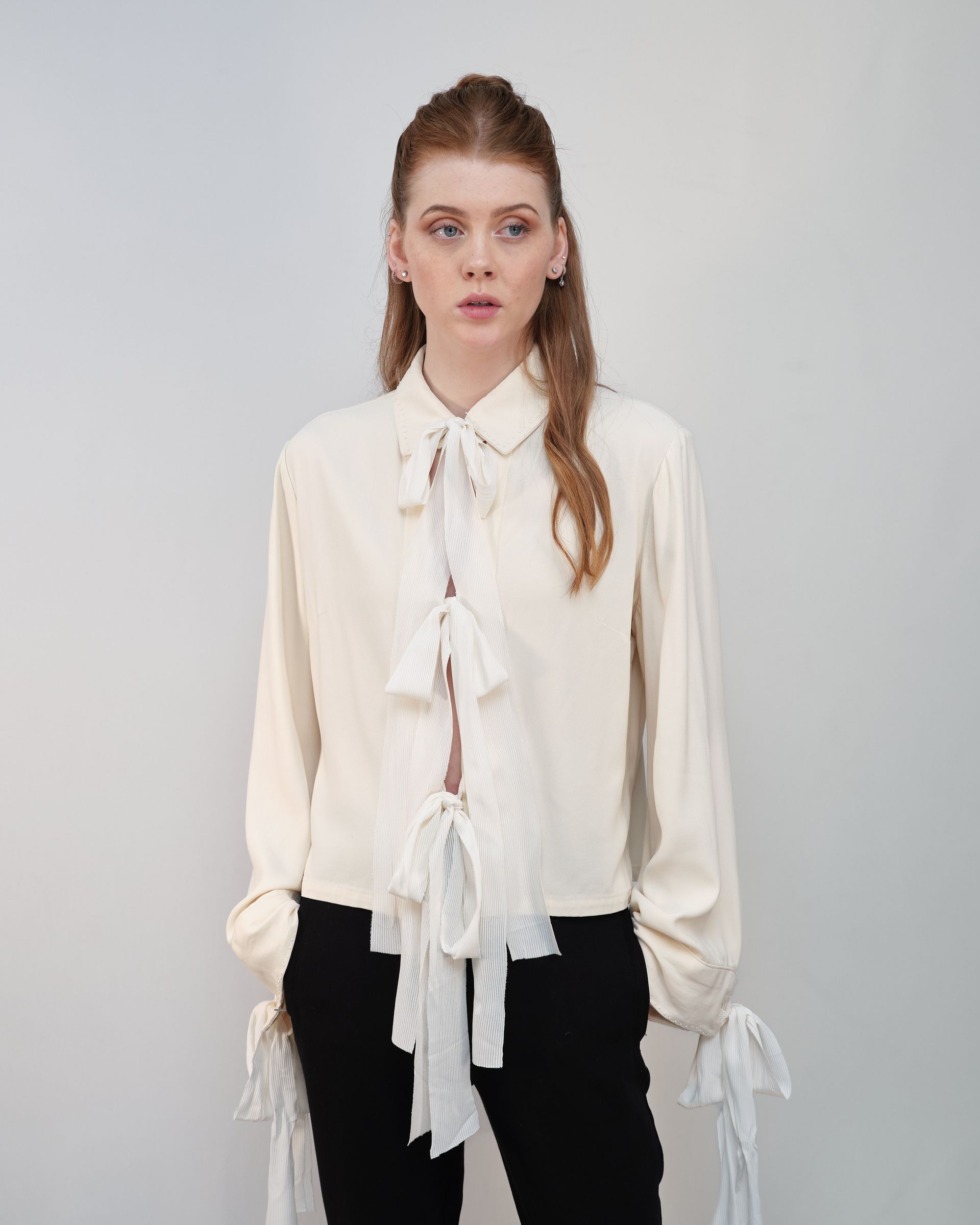 A woman is wearing a white shirt with a bow and black pants.