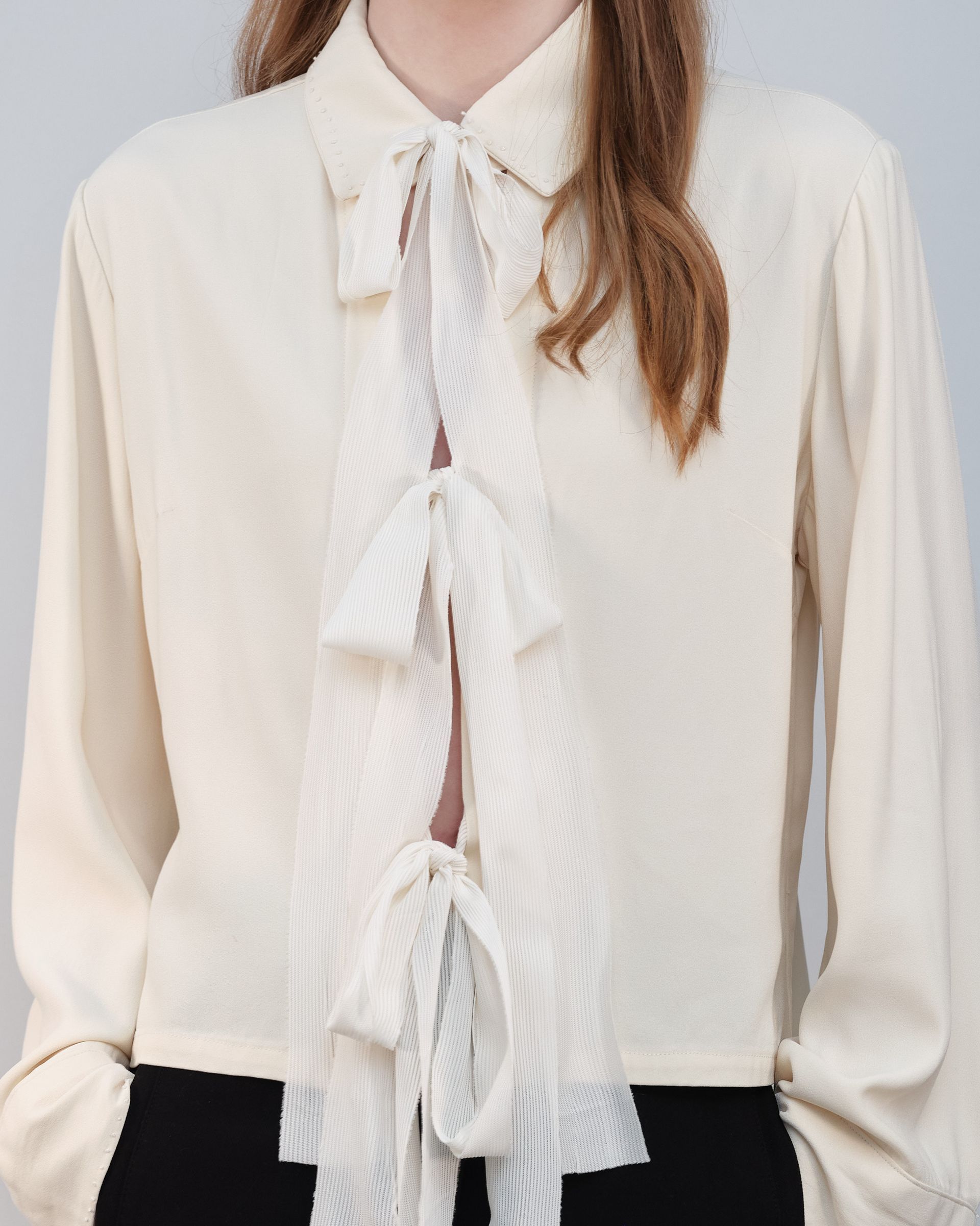 A woman is wearing a white shirt with a lace tie around her neck