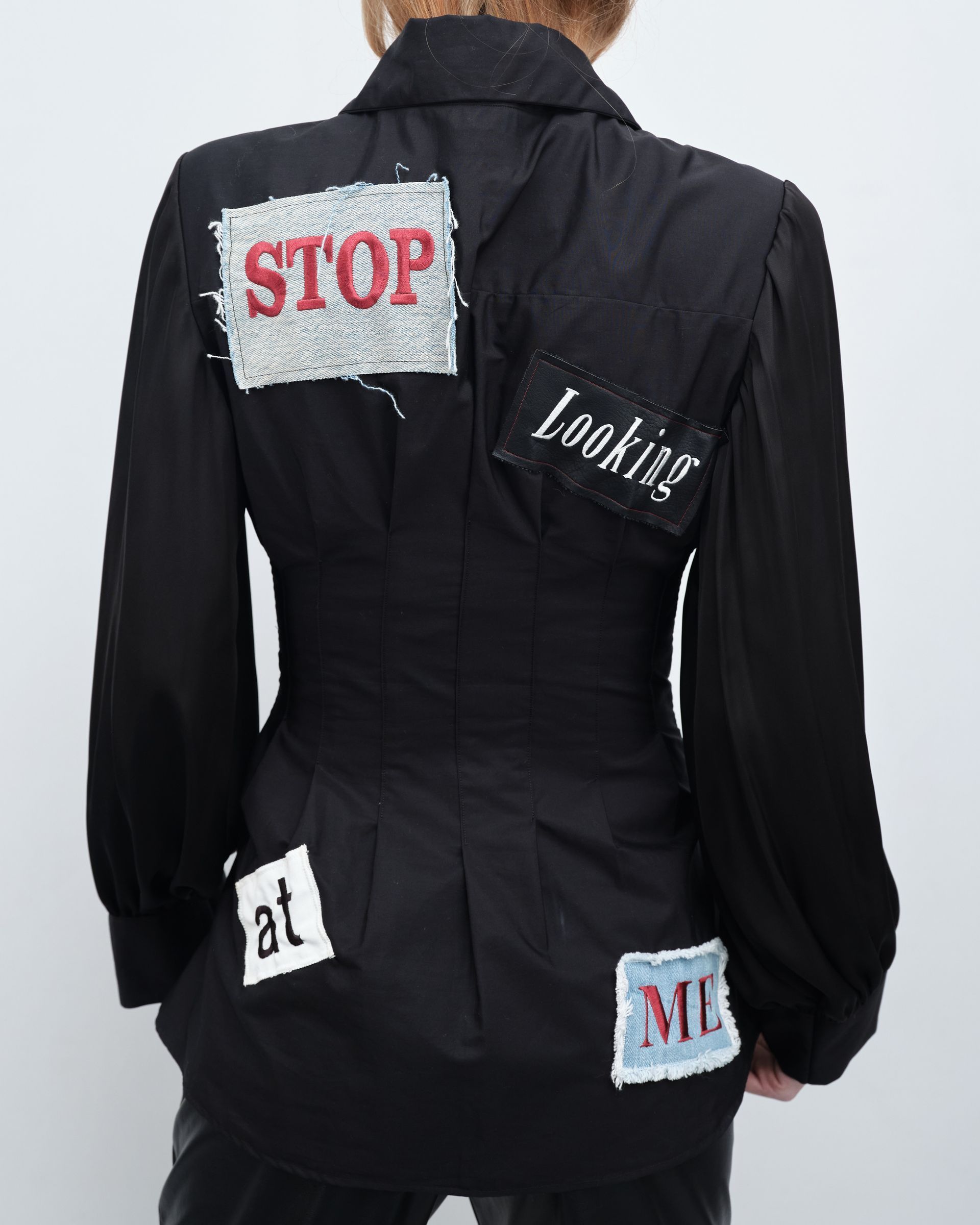 A woman wearing a black jacket with patches on the back that say stop looking at me