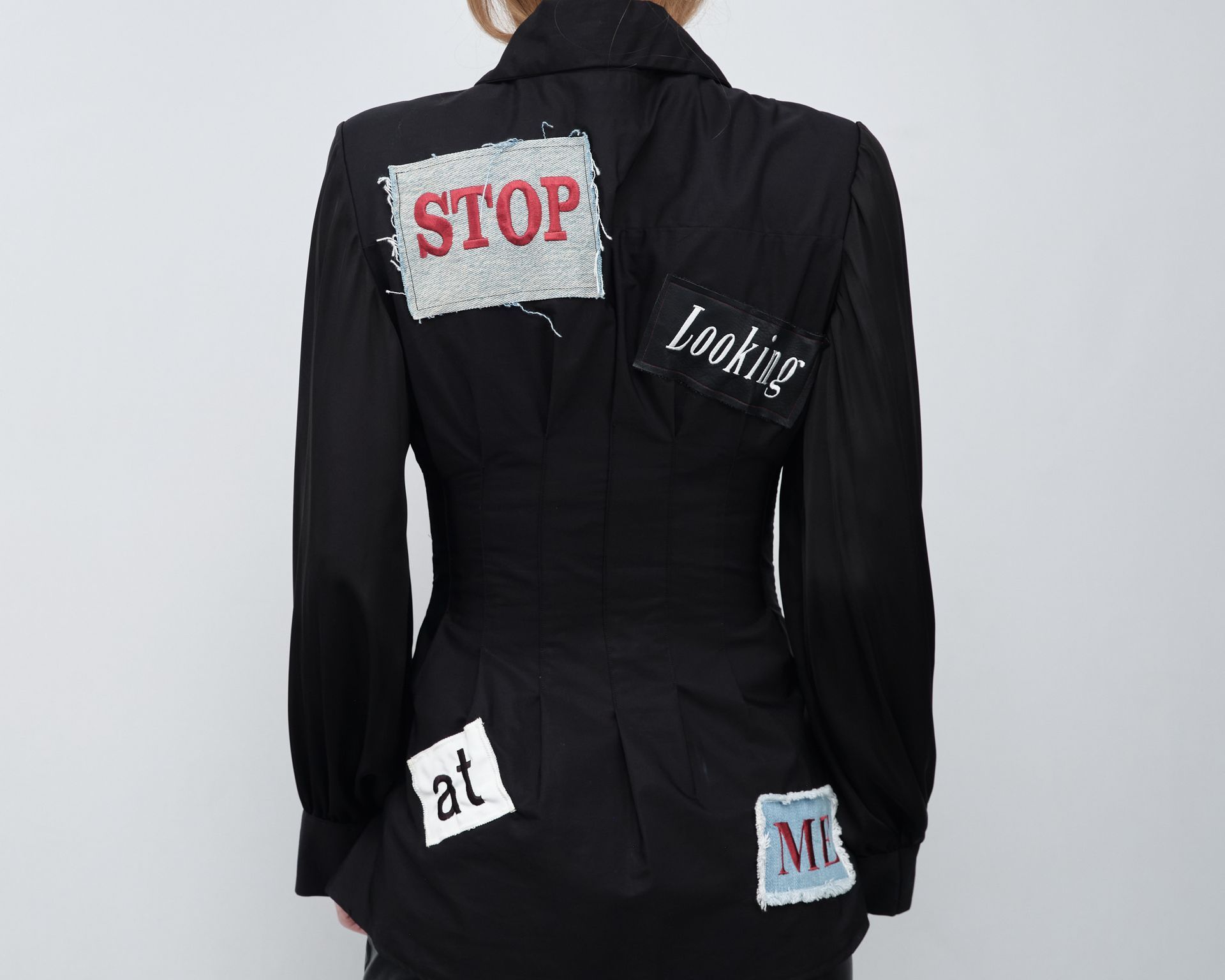 A woman wearing a black jacket with patches that say stop looking at me