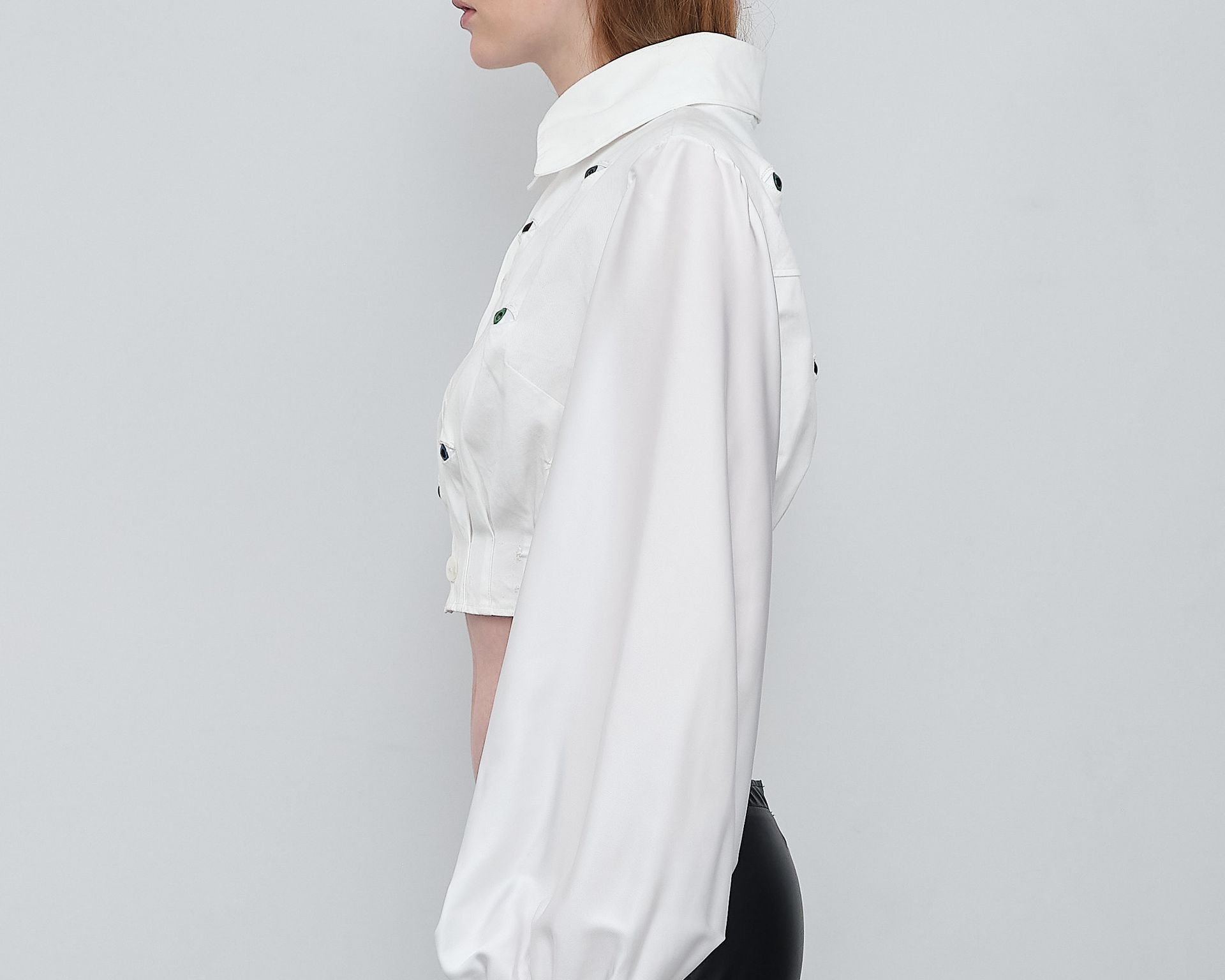 A woman is wearing a white shirt with puffed sleeves and black pants.