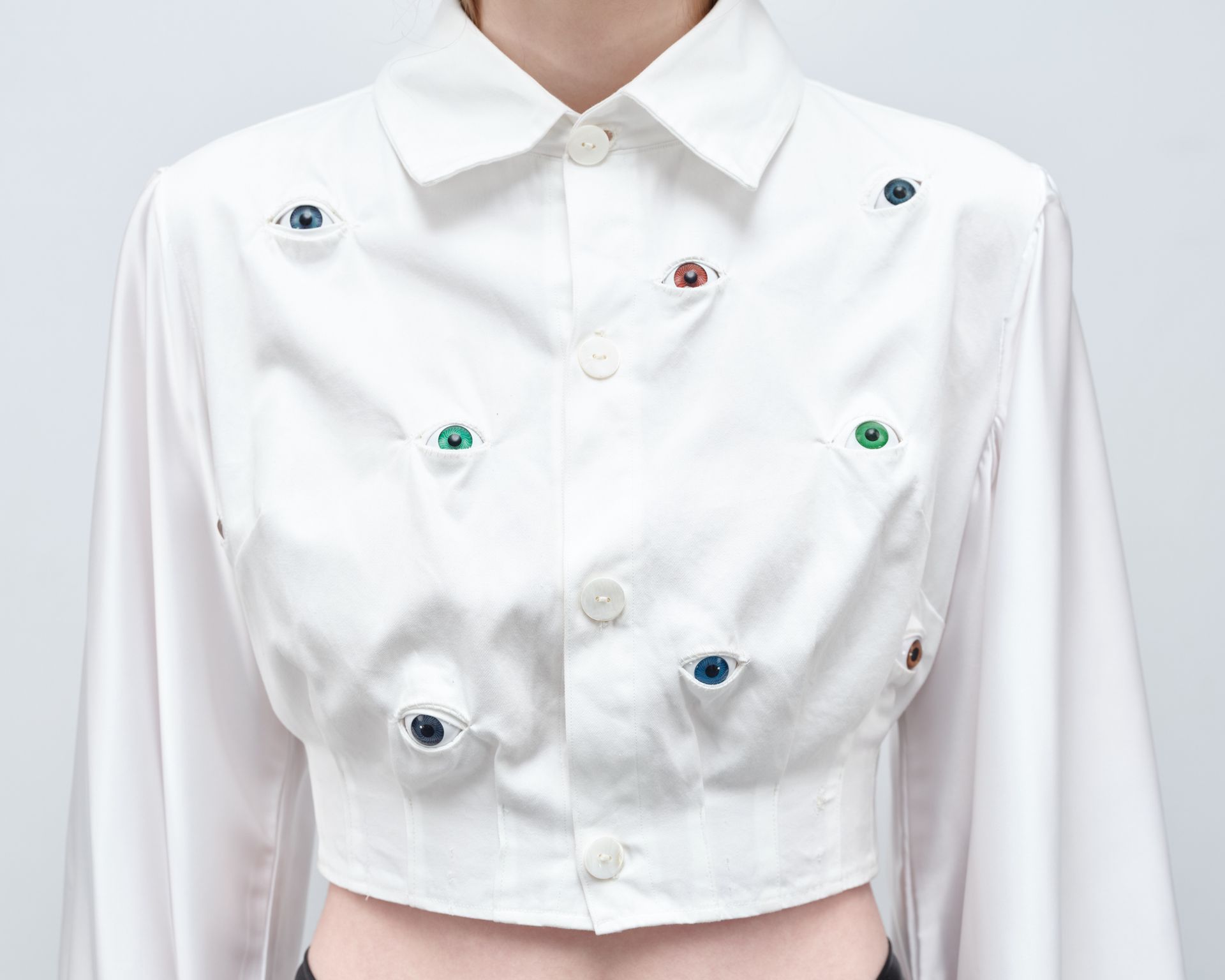 A woman is wearing a white shirt with eyes embroidered on it.