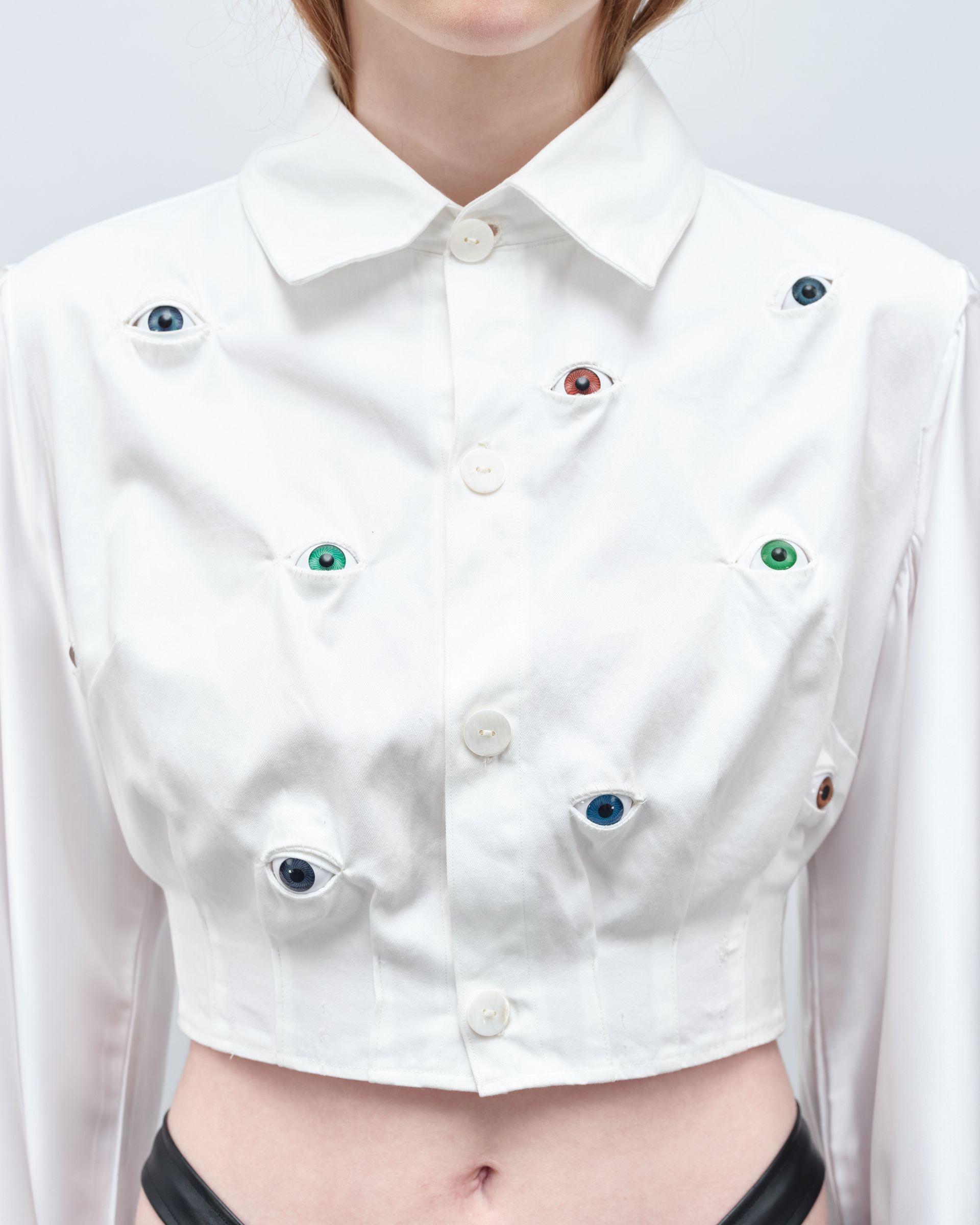 A woman is wearing a white shirt with eyes embroidered on it.