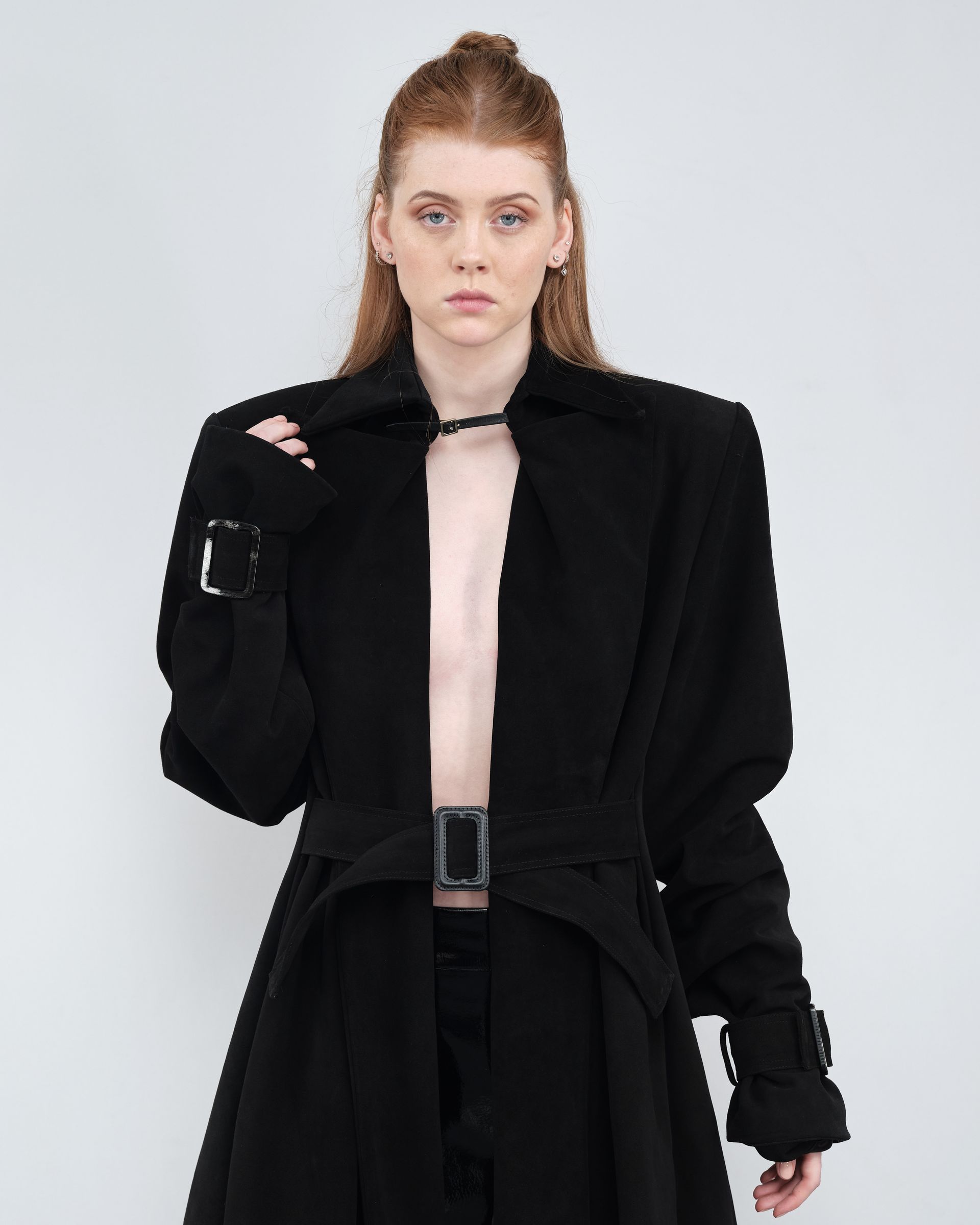A woman without a shirt is wearing a black coat