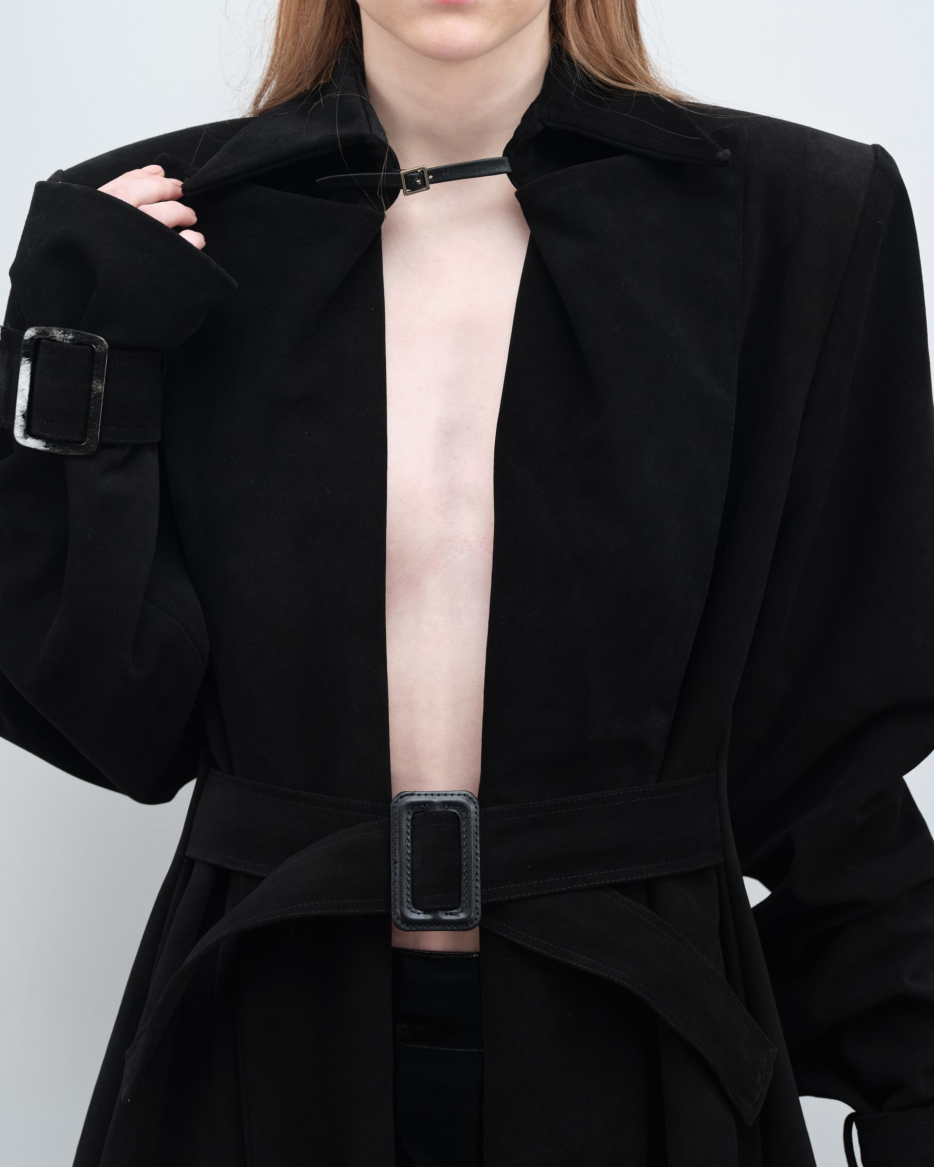 A woman without a shirt is wearing a black coat