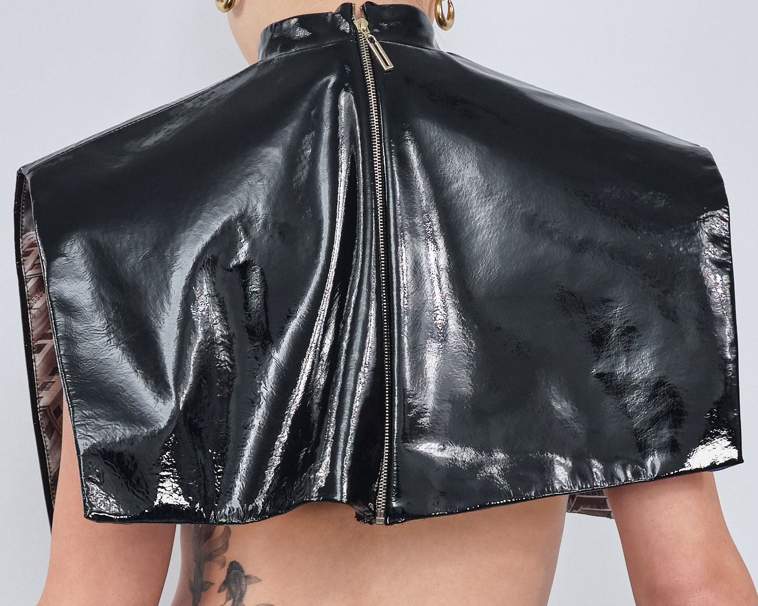 A woman with a tattoo on her back is wearing a black leather cape